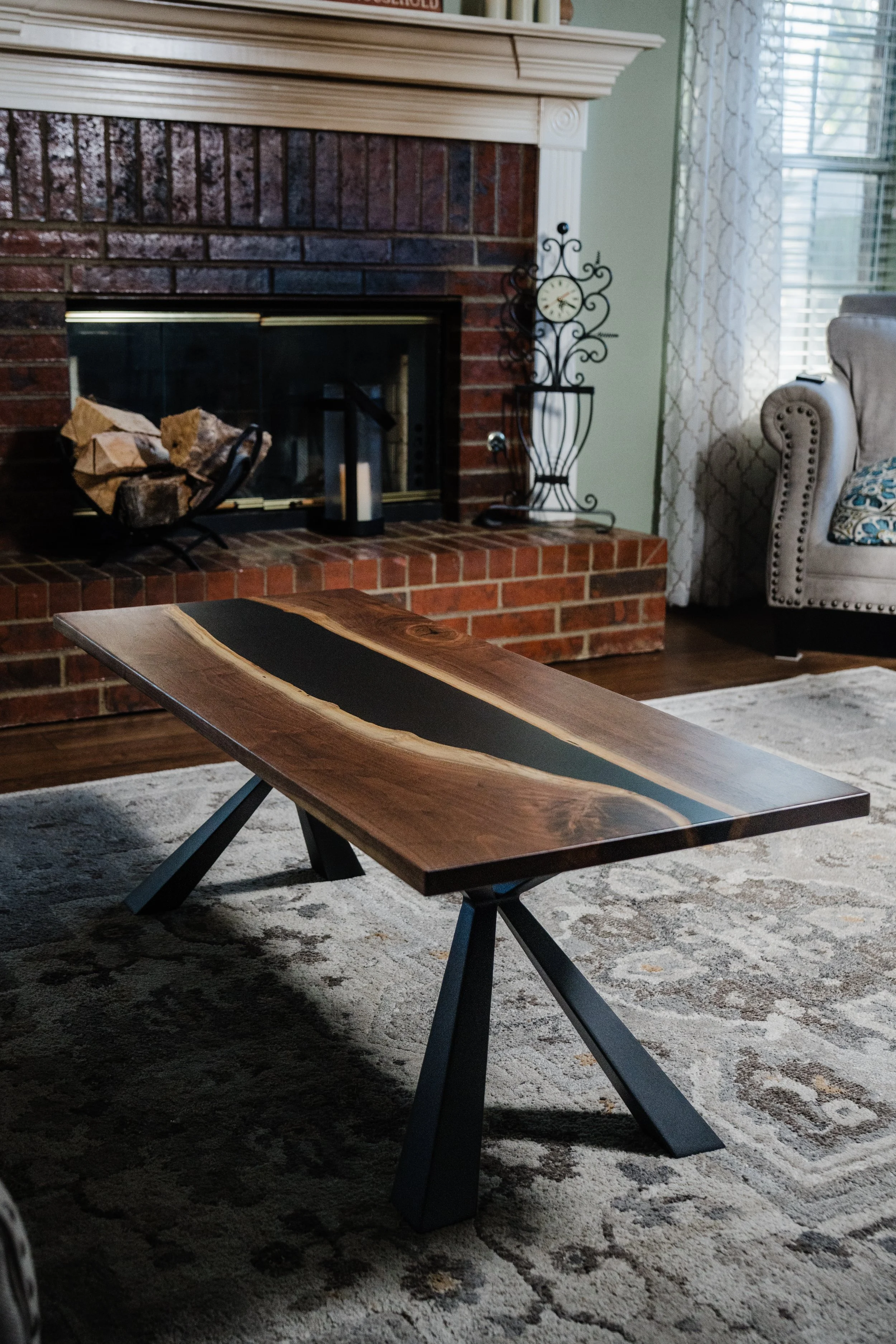 A wooden coffee table with a black inlay on top in front of a brick fireplace in a cozy living room.