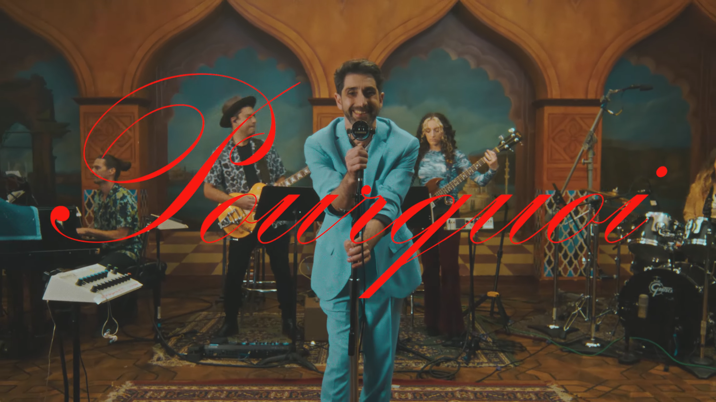 A man in a light blue suit singing into a microphone in a band with various instruments, including guitars, keyboards, and drums, in a decorated indoor setting with wooden arches and painted walls. The word 'Promotion' is written in large red cursive across the image.