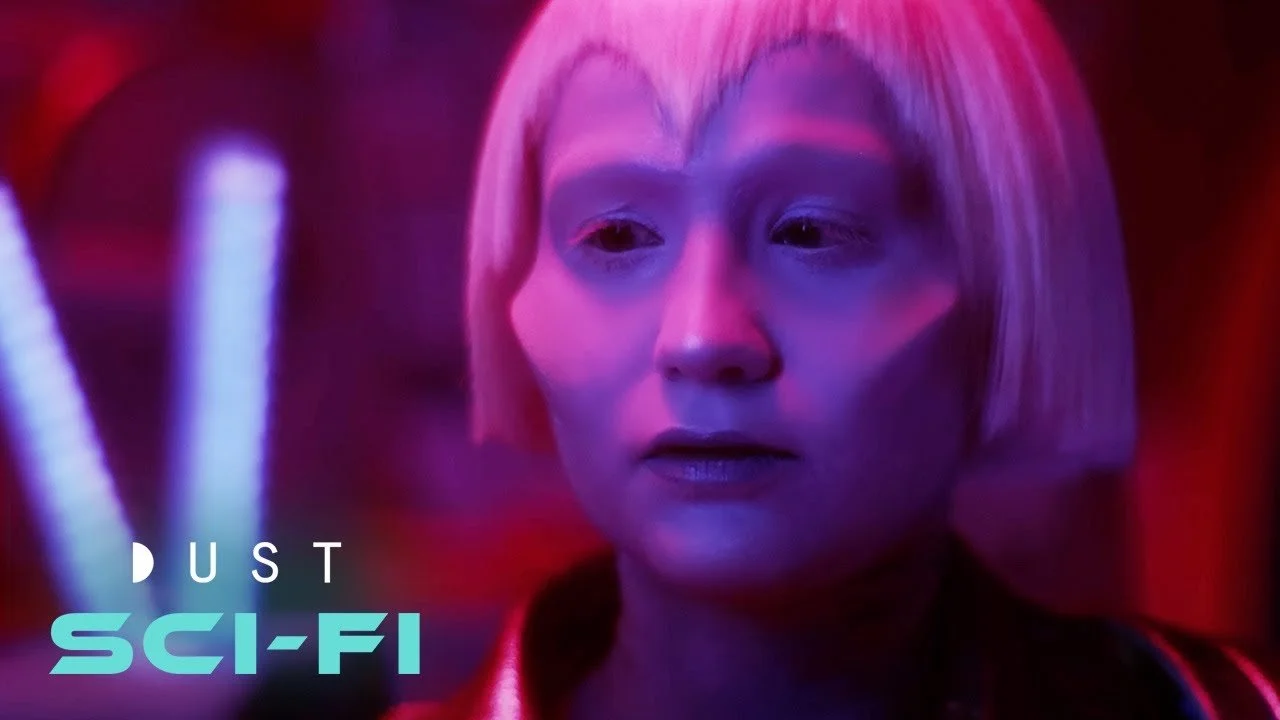 A woman with short blonde hair looking intently, illuminated by purple and red neon lights, with the text 'DUST SCI-FI' in the lower left corner.