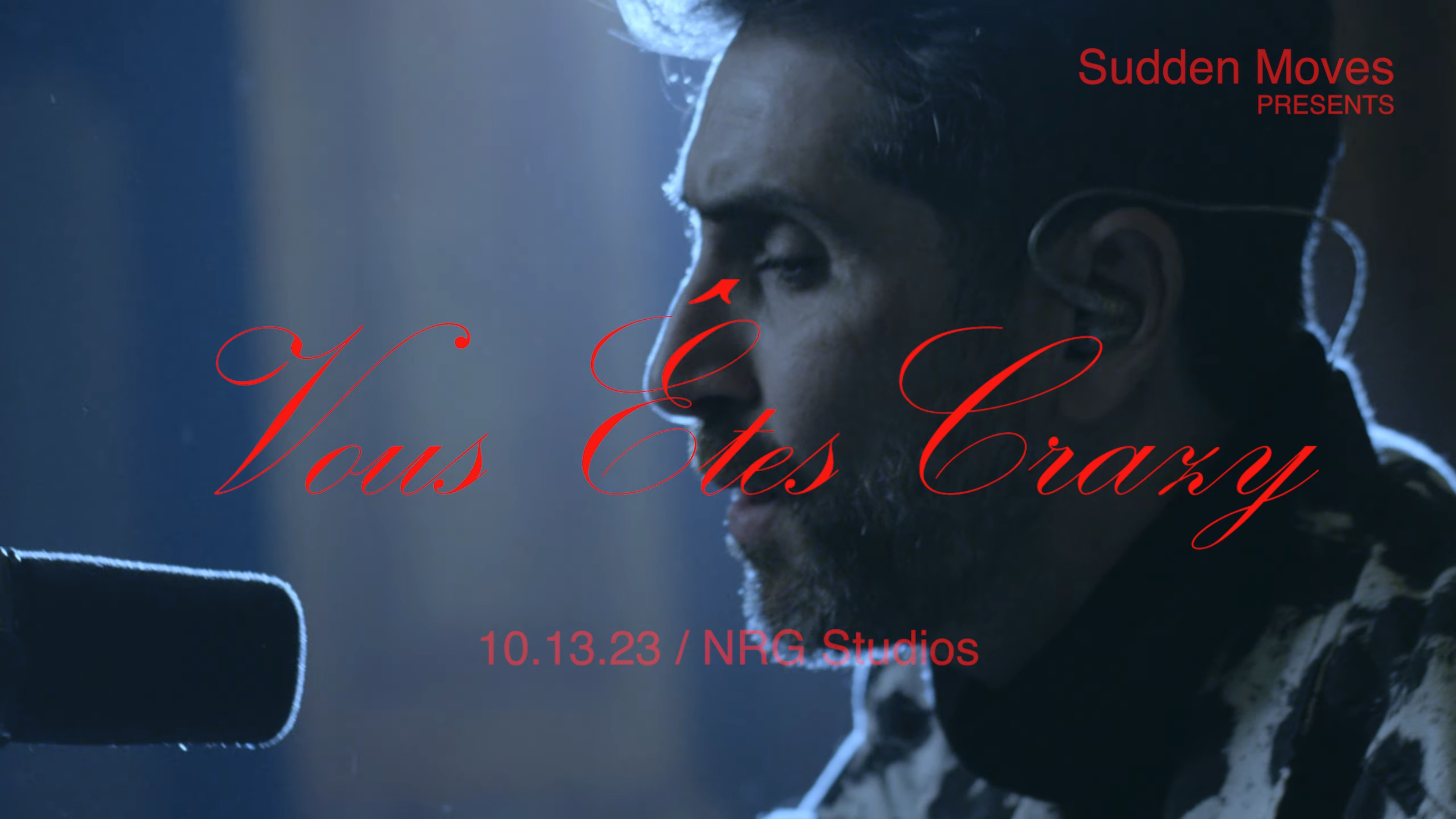 Close-up of a man with dark hair and a beard, speaking into a microphone, with a dark background and overlaying red text promoting a film titled "Vous Êtes Cruzx," presenting on October 13, 2023, at NRG Studios, produced by Sudden Moves.