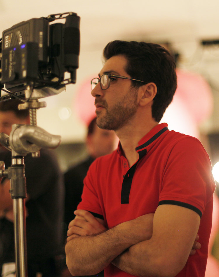Filmmaker using a camera stabilizer rig during a shoot in a brightly lit room, with another crew member standing in the background.