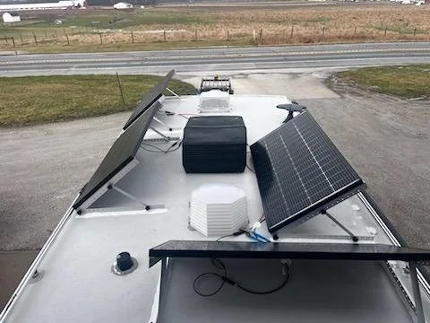 Solar panels mounted on the roof of a mobile vehicle, with a black object and a white vent visible, outside near a road.