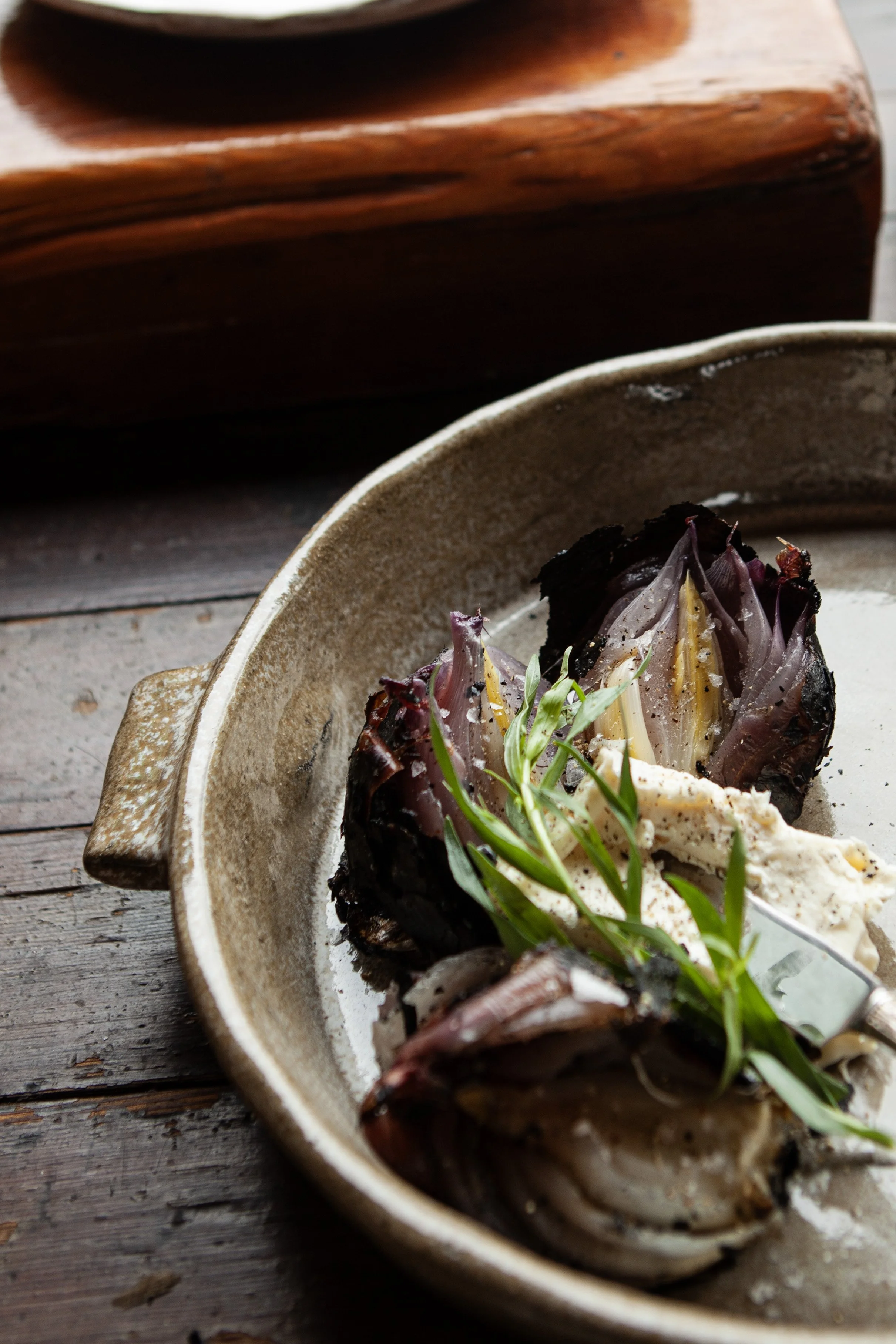 A ceramic bowl filled with cooked fish, garnished with green herbs on a rustic wooden surface.