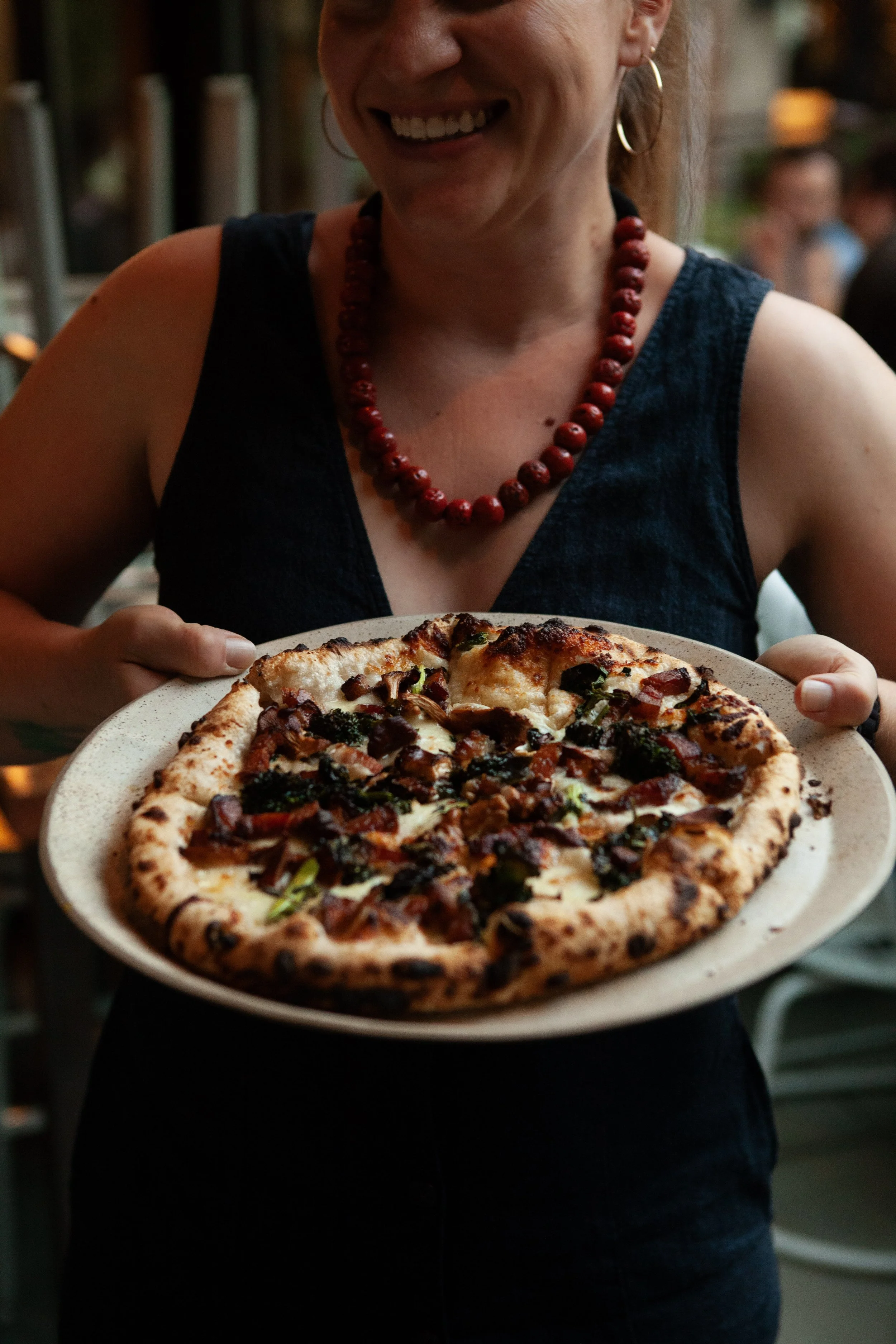 A woman is smiling and holding a plate of pizza.