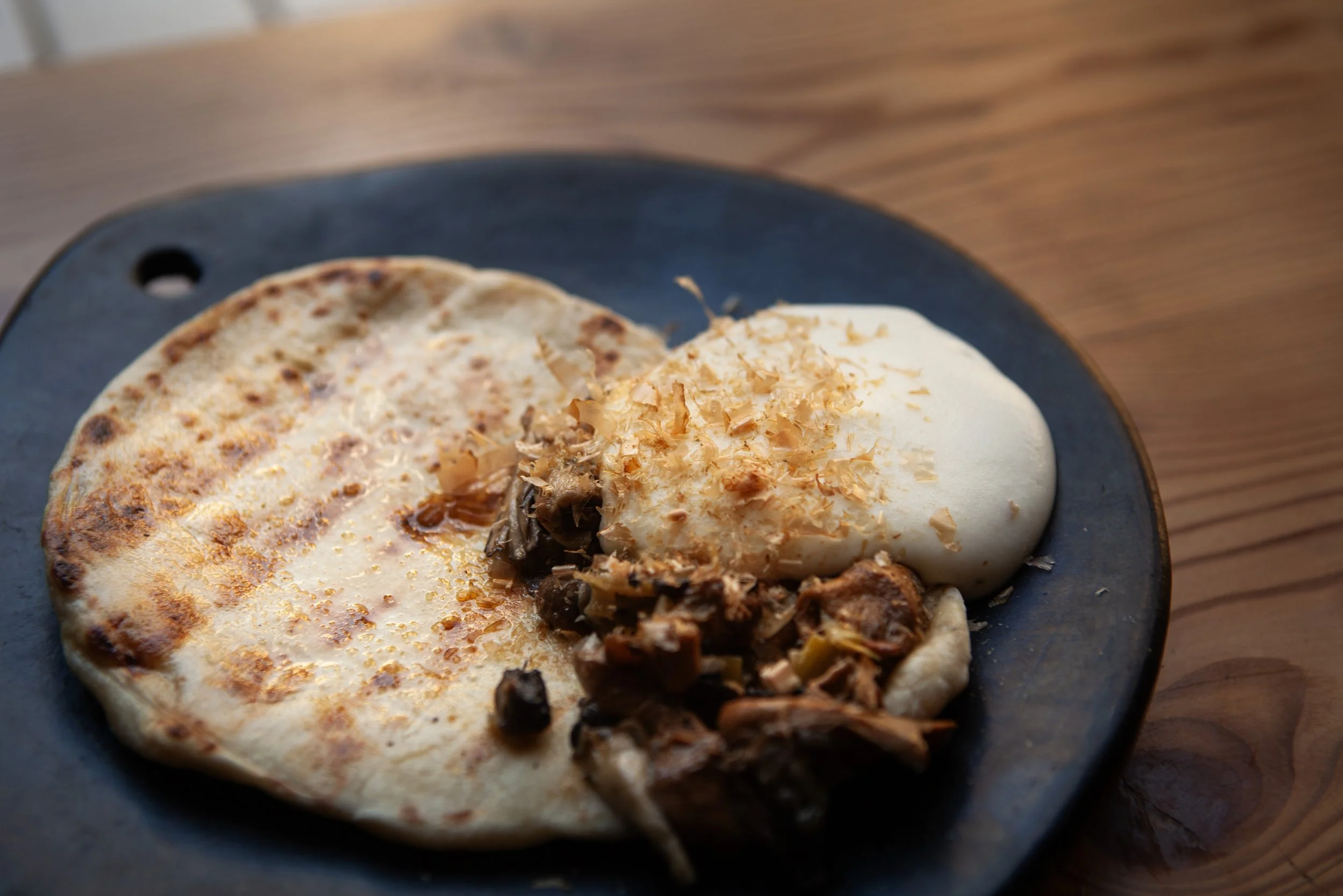 A plate with a fried egg, shredded cheese, and seasoned meat on a black ceramic dish placed on a wooden surface.