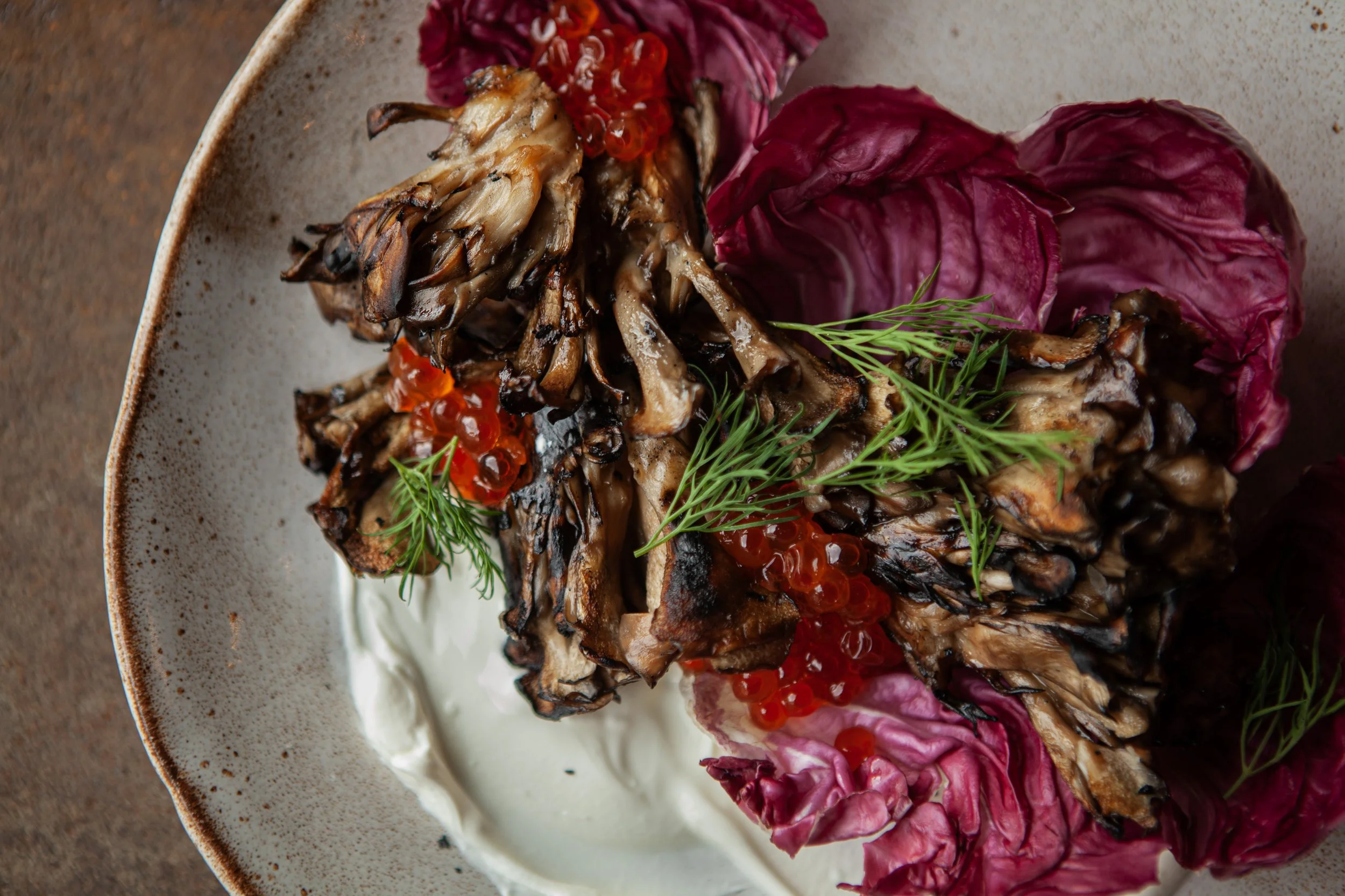 Grilled chicken served with red caviar, fresh dill, and purple radicchio leaves on a white plate.
