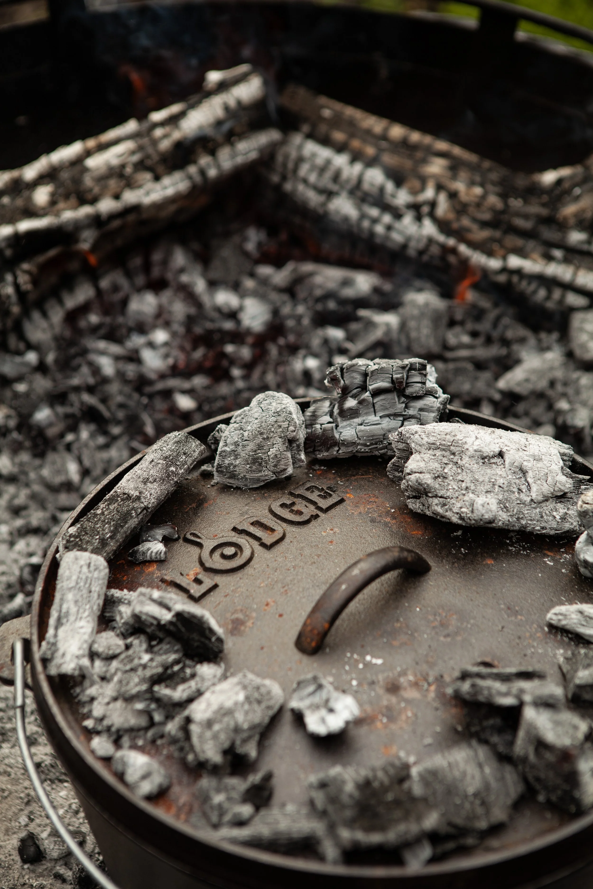 Charcoal ashes and partially burnt wood in a metal container, with a background of more ashes and burnt wood.