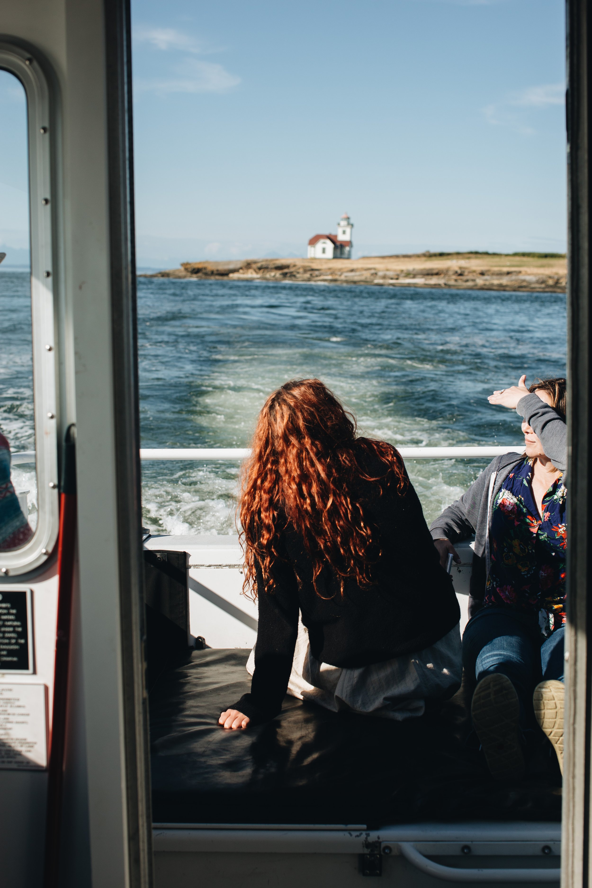 People are sitting on a boat enjoying a scenic view of water and a lighthouse on a small island.