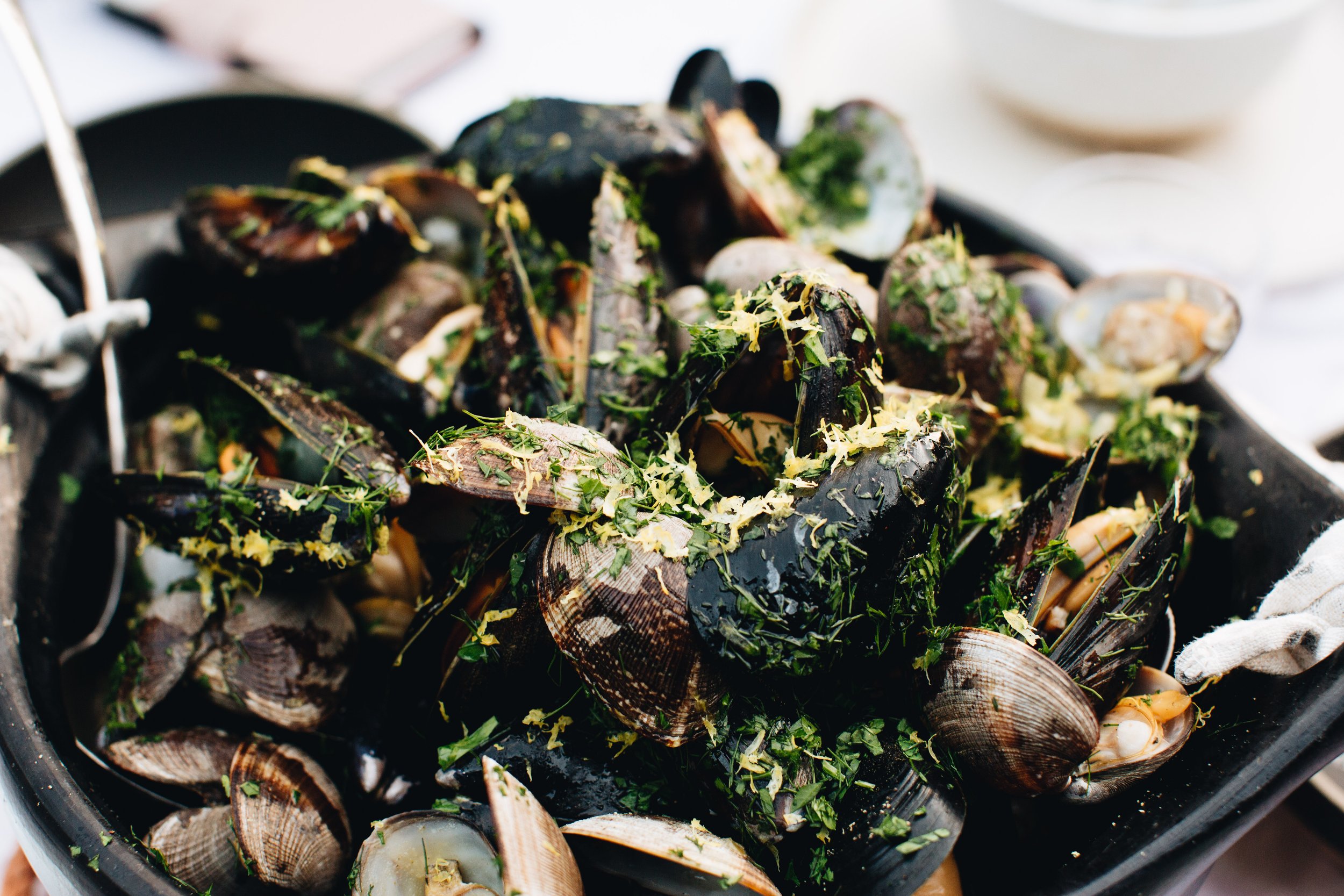 A black dish filled with cooked mussels topped with chopped herbs and lemon zest.