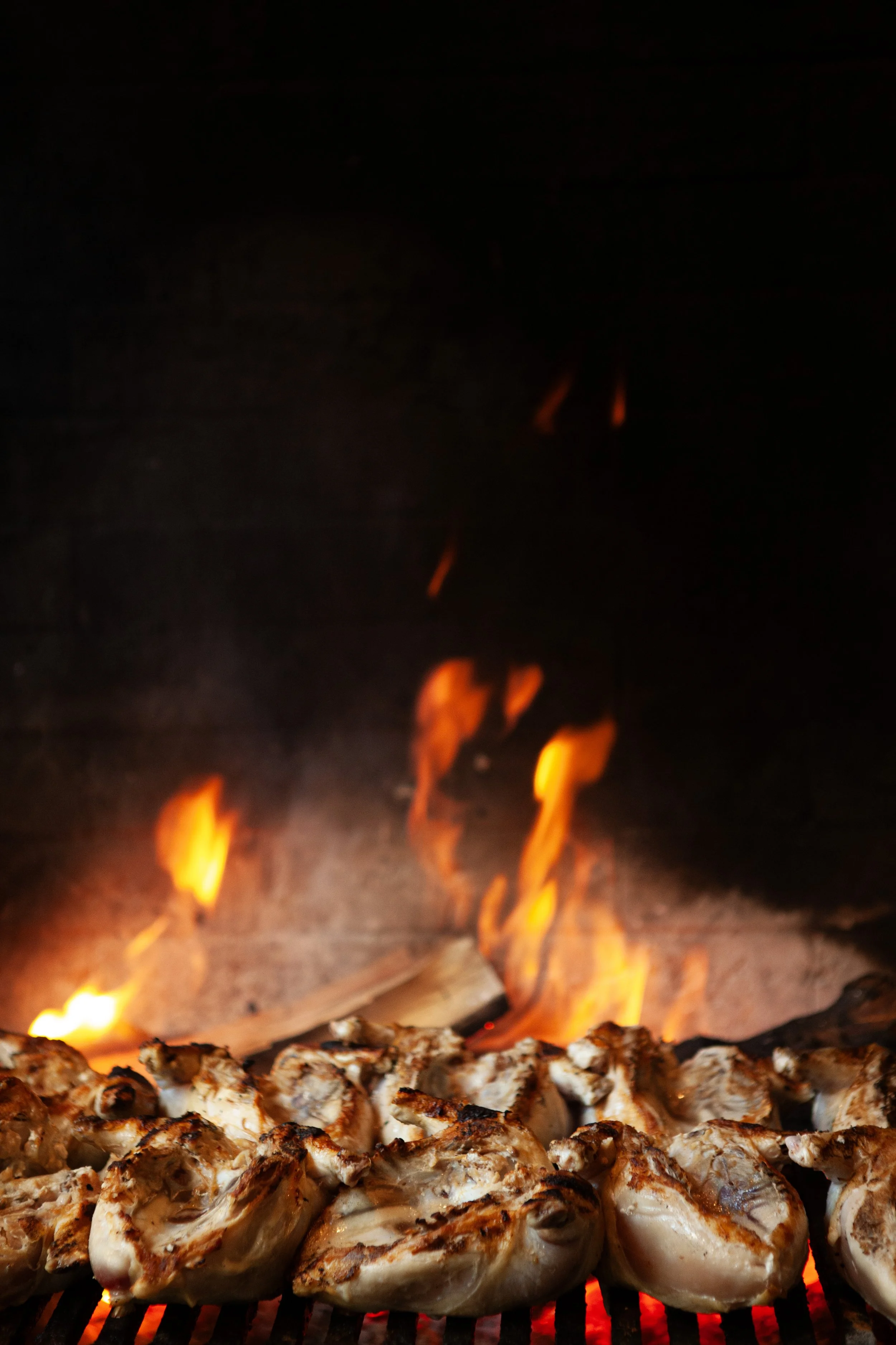 Chicken grilling over open flame in a barbecue oven.