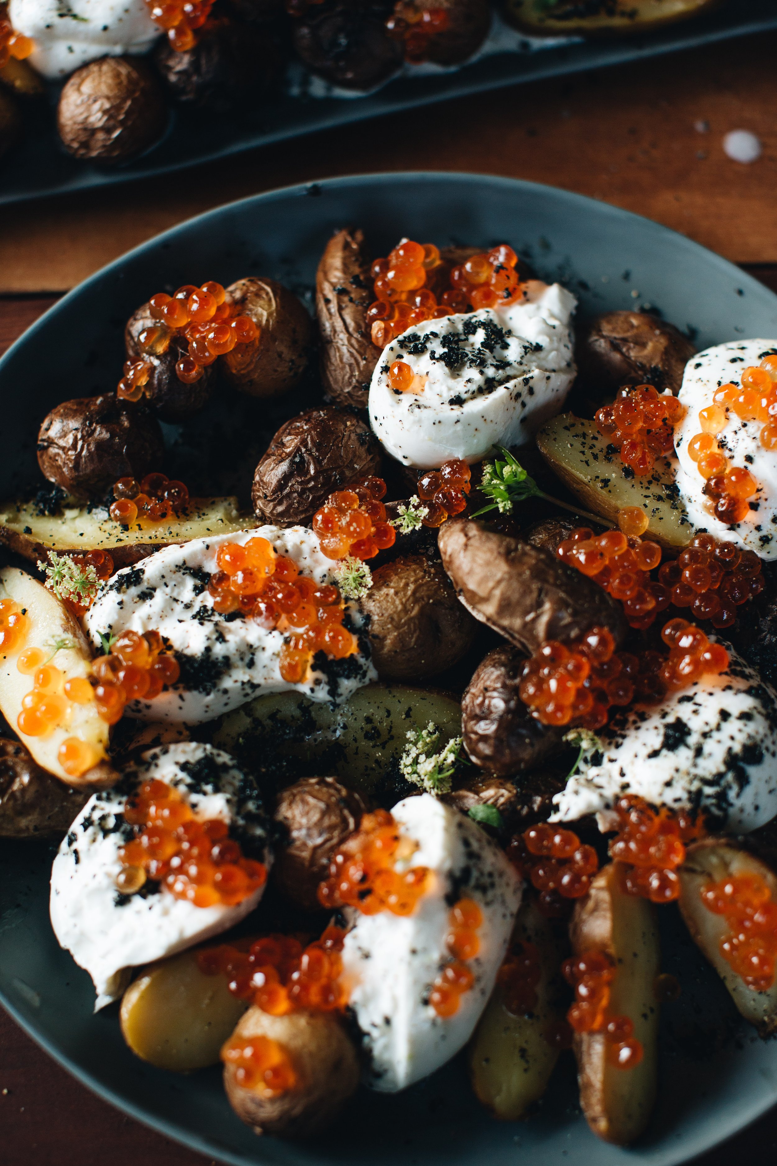 A plate of roasted potatoes topped with sour cream, red caviar, and black pepper, garnished with herbs.