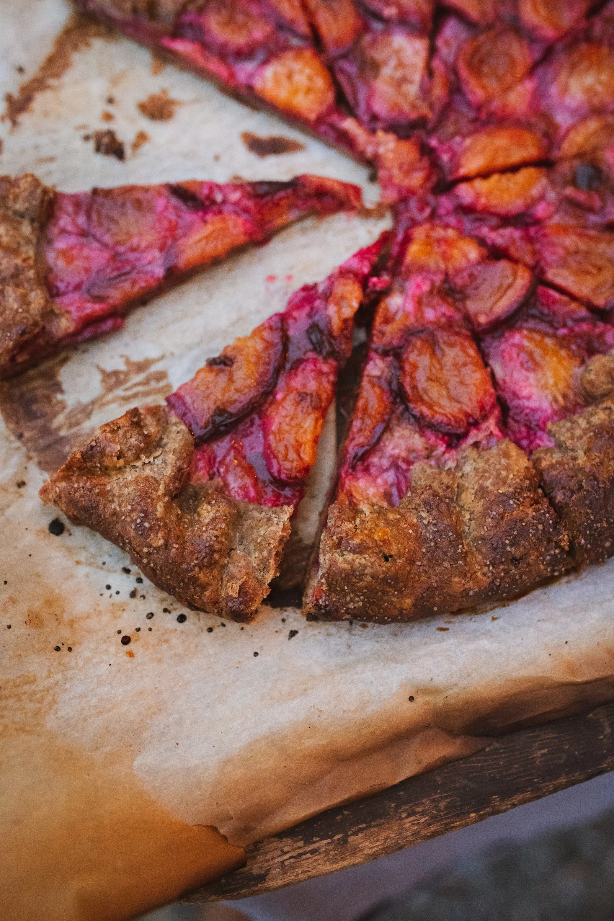 Close-up of a sliced homemade apple pie with a golden, crumbly crust and apple slices inside, resting on parchment paper.