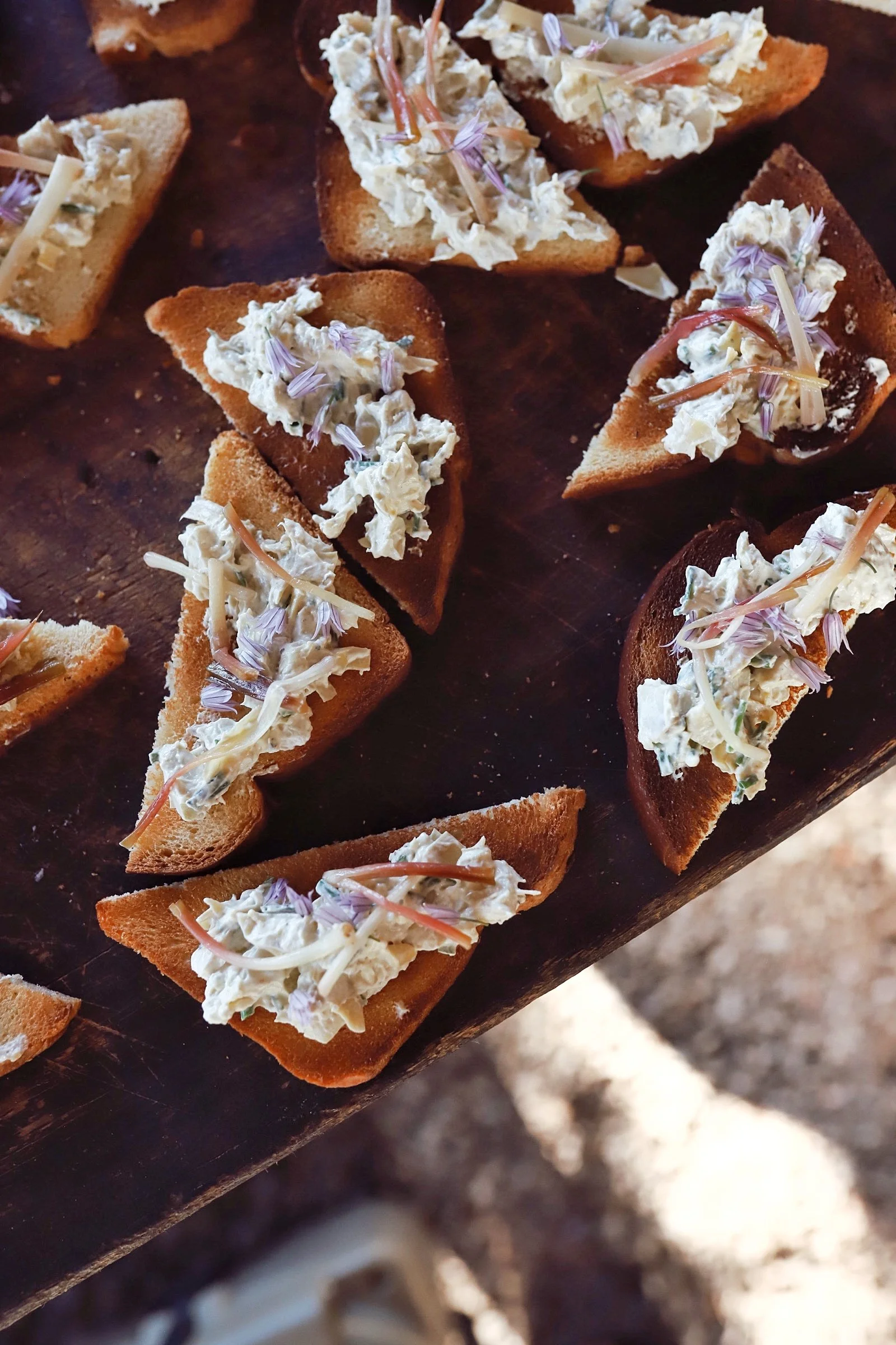 Close-up of toasted bread slices topped with creamy cheese, shredded cheese, and edible flower petals.