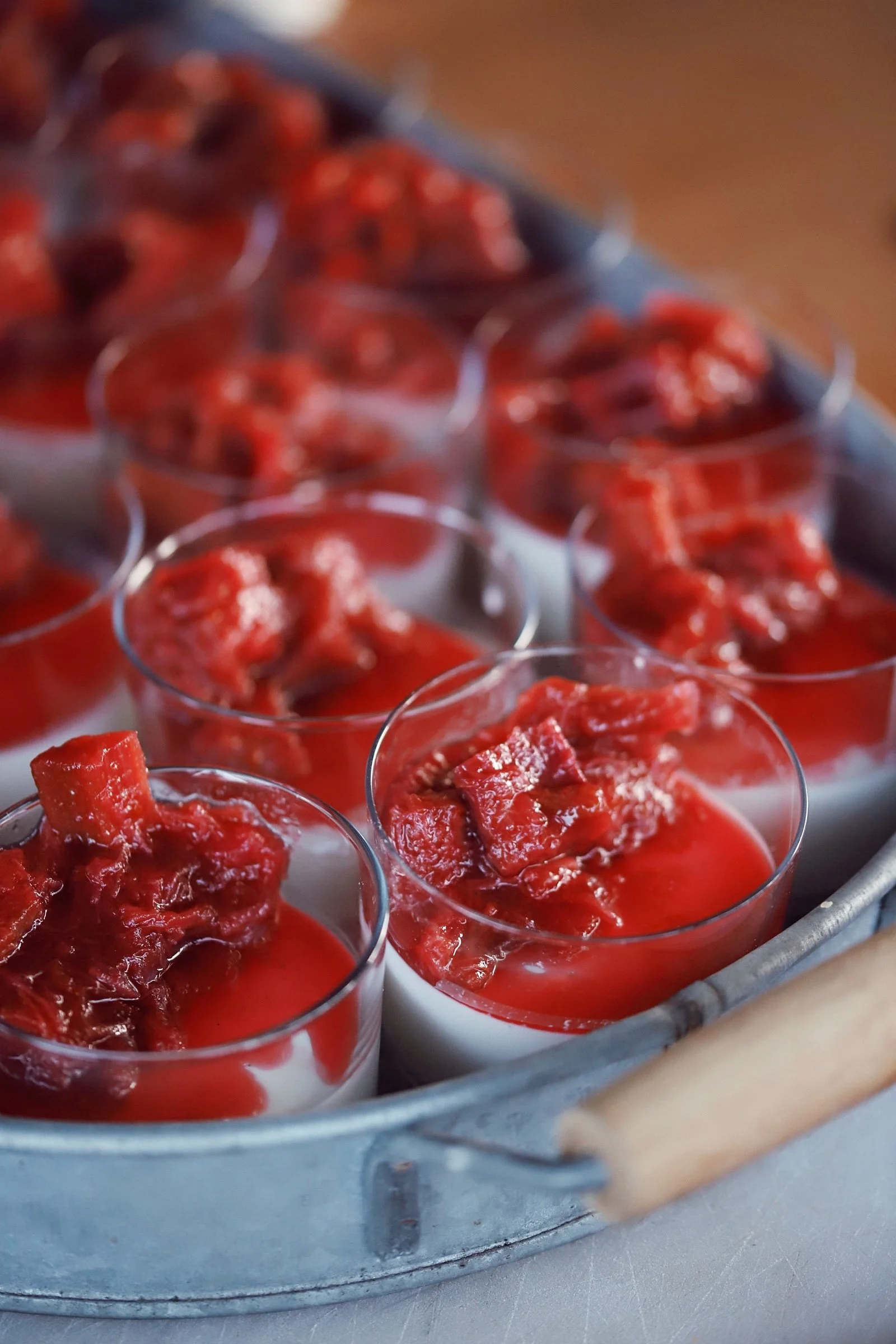 Mini desserts in clear cups with a layer of white cream and topped with red fruit compote, arranged in a tray.
