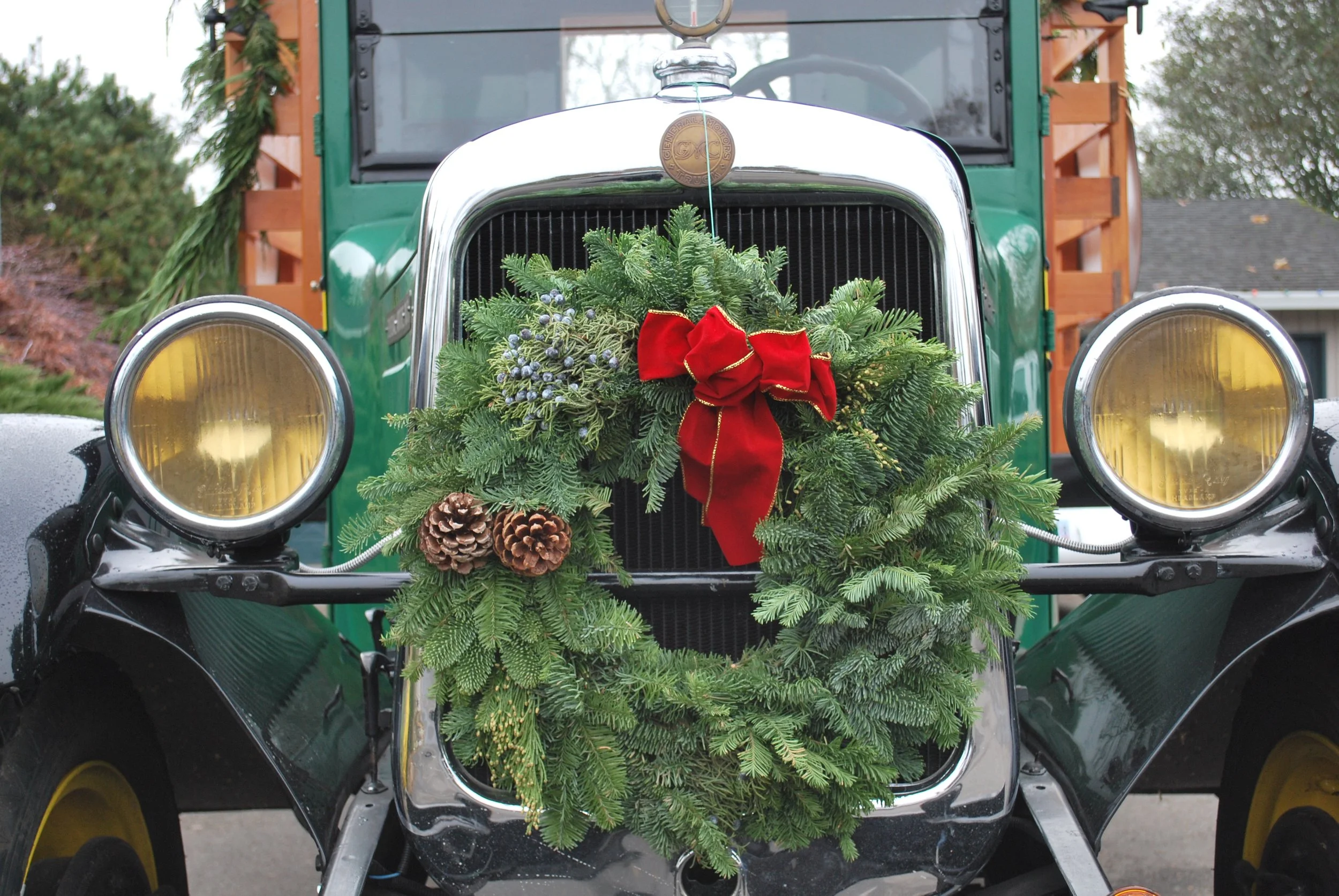 Front of vintage truck decorated with Christmas greenery, pinecones, and a red bow.