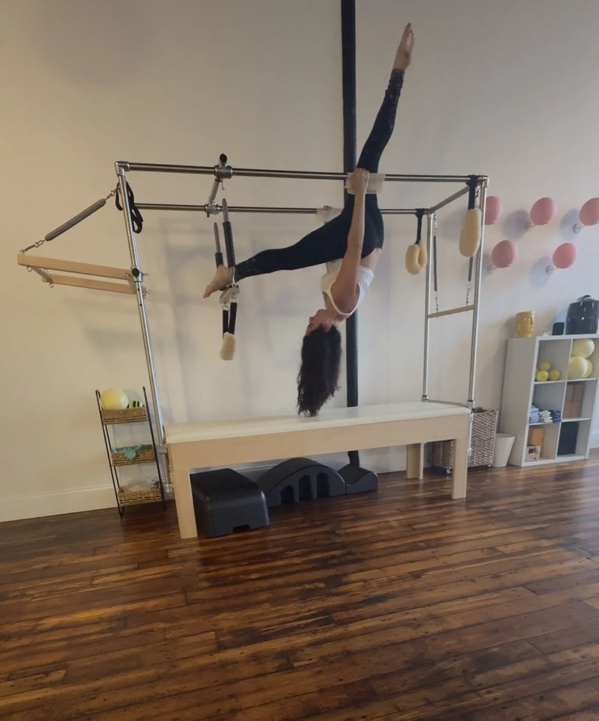 A woman practicing pilates on the Cadillac inside a studio with wooden floors.