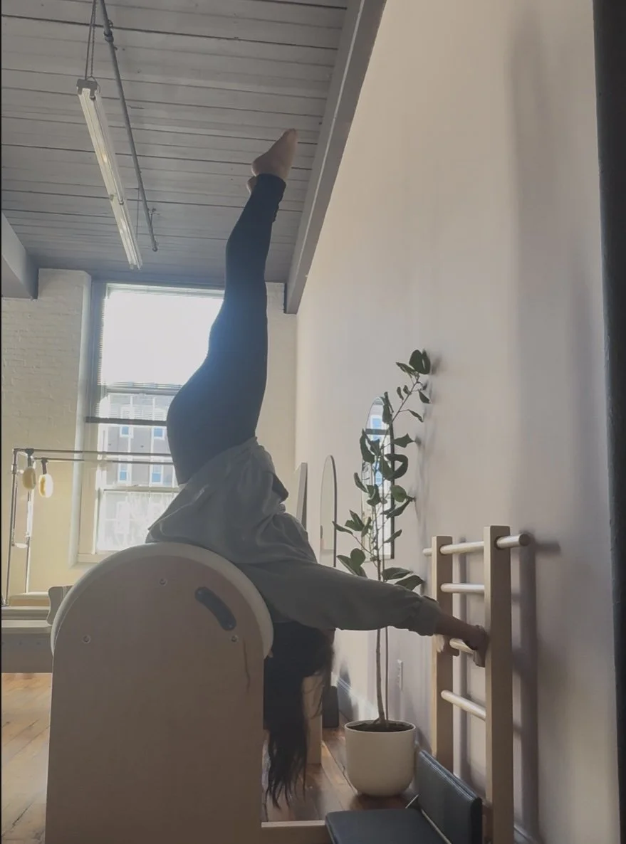 Person performing a shoulder stretch or exercise using a ladder barrel in a bright room with large windows and a plant.
