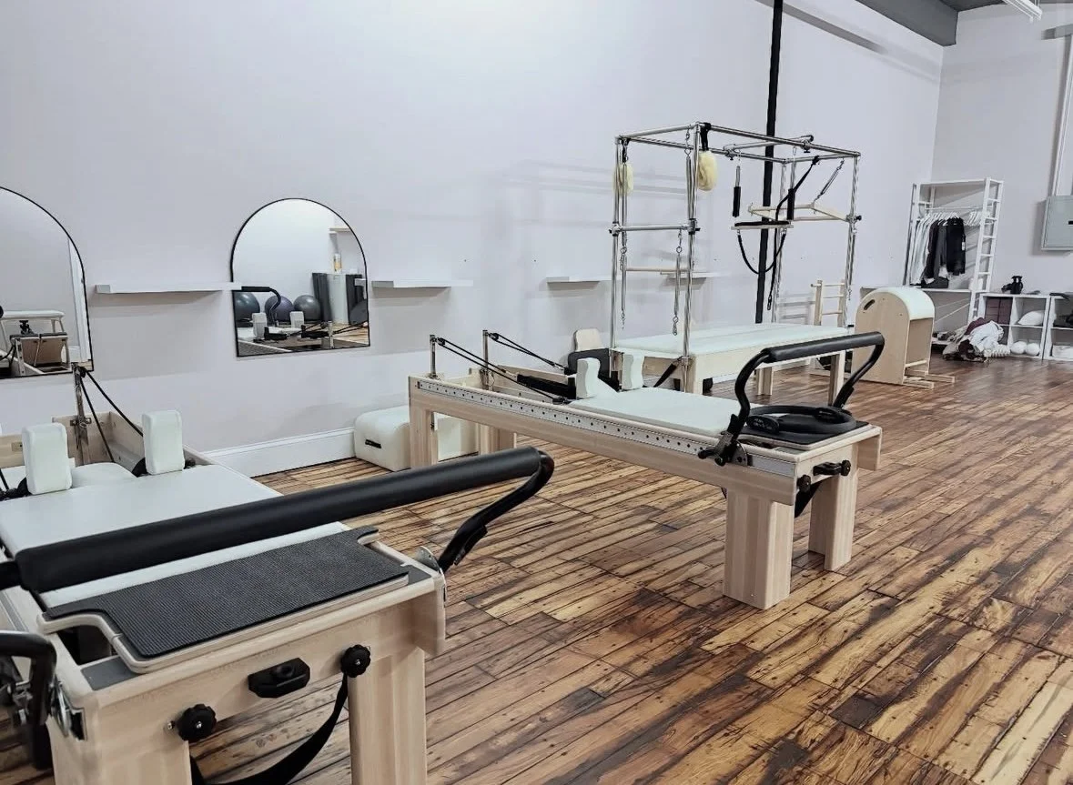 Pilates studio with reformer machines, exercise equipment, large mirrors, and wooden flooring.