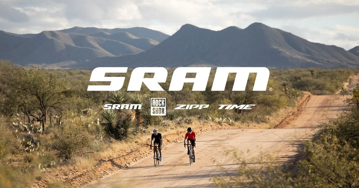 Two cyclists riding on a dirt trail in a desert landscape with mountains in the background, overlaid with the text 'SRAM' and related brand logos.