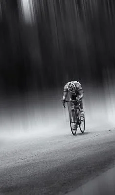 Cyclist riding on a road with a forested backdrop in black and white.