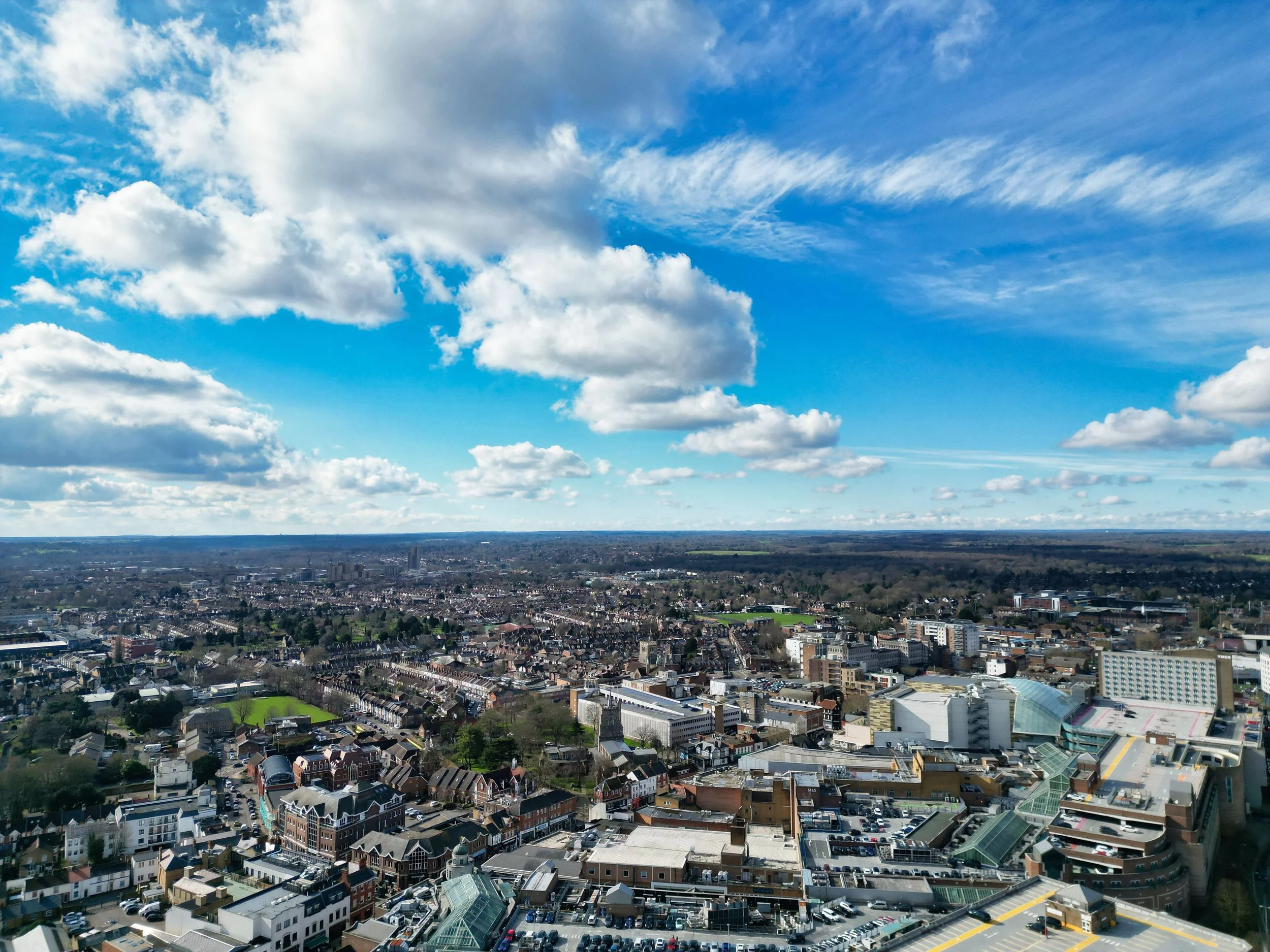 Aerial view of a cityscape with residential and commercial buildings under a partly cloudy sky.