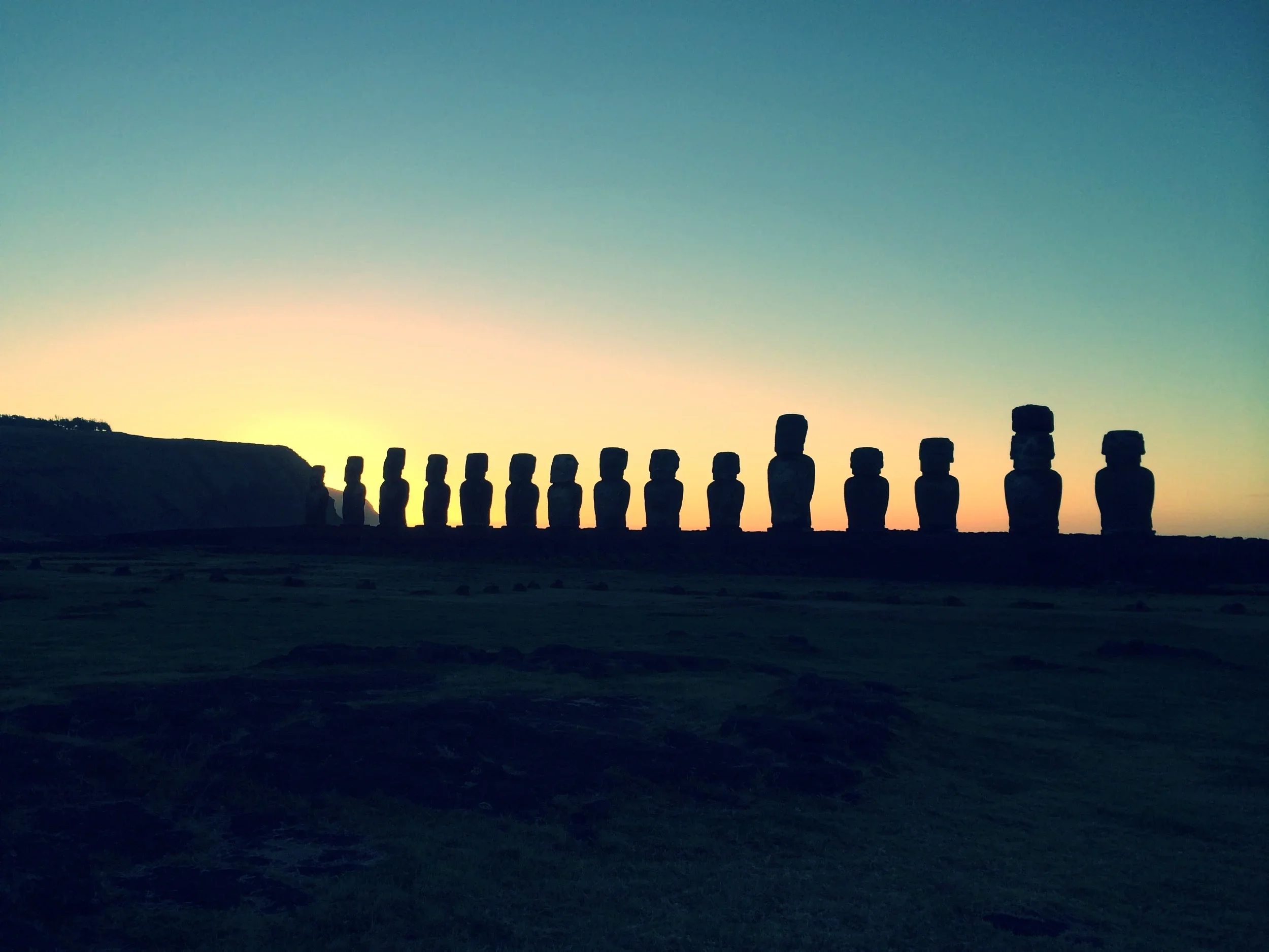 Silhouettes of Moai statues on Easter Island against a sunset sky.