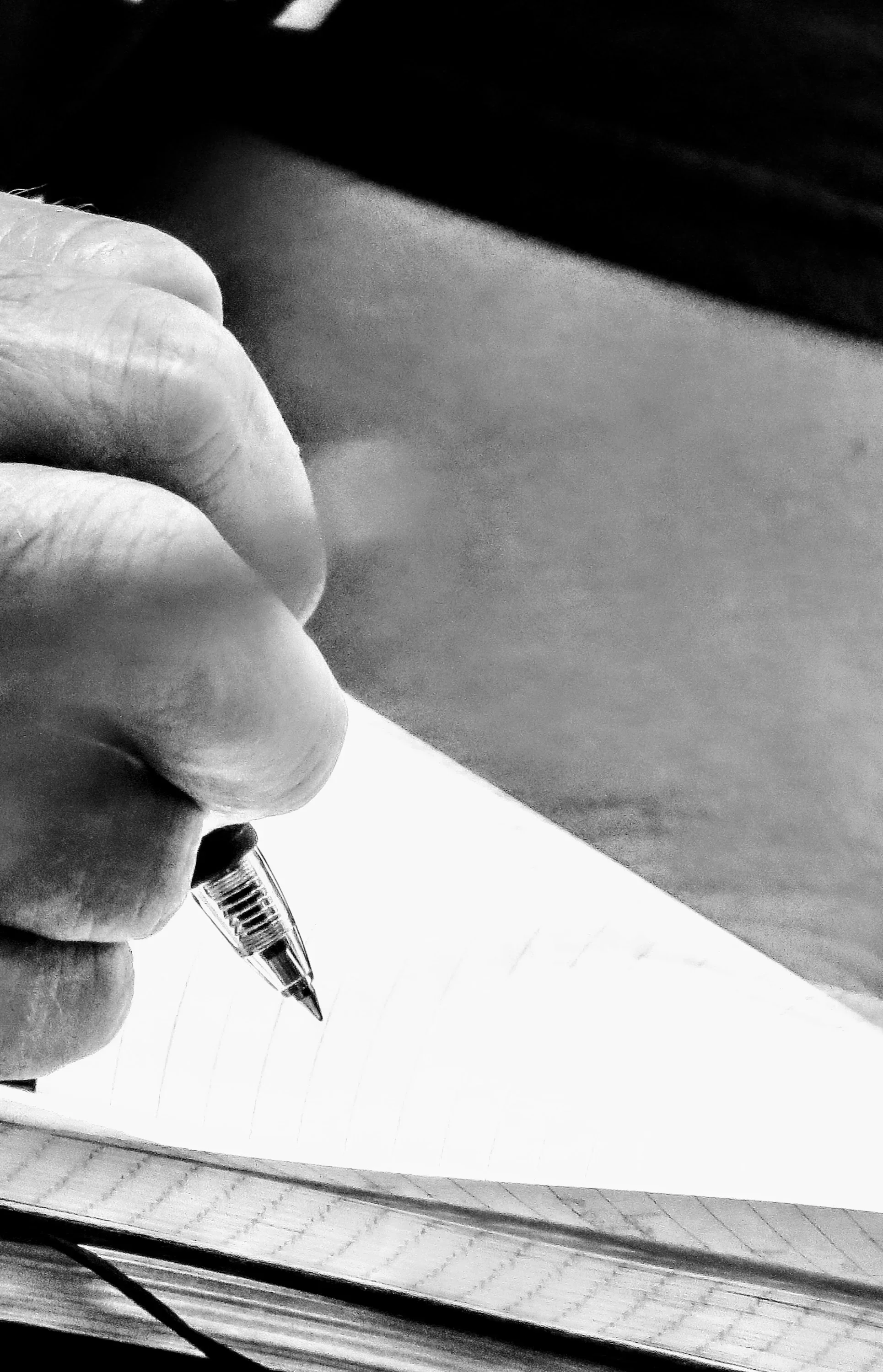 Close-up of a hand holding a pen writing on a lined piece of paper on a desk.
