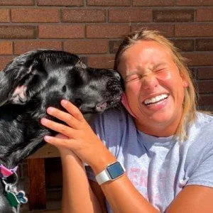 Taylor and a black dog licks her face