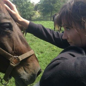 Tami gently touching a horse's head outdoors.