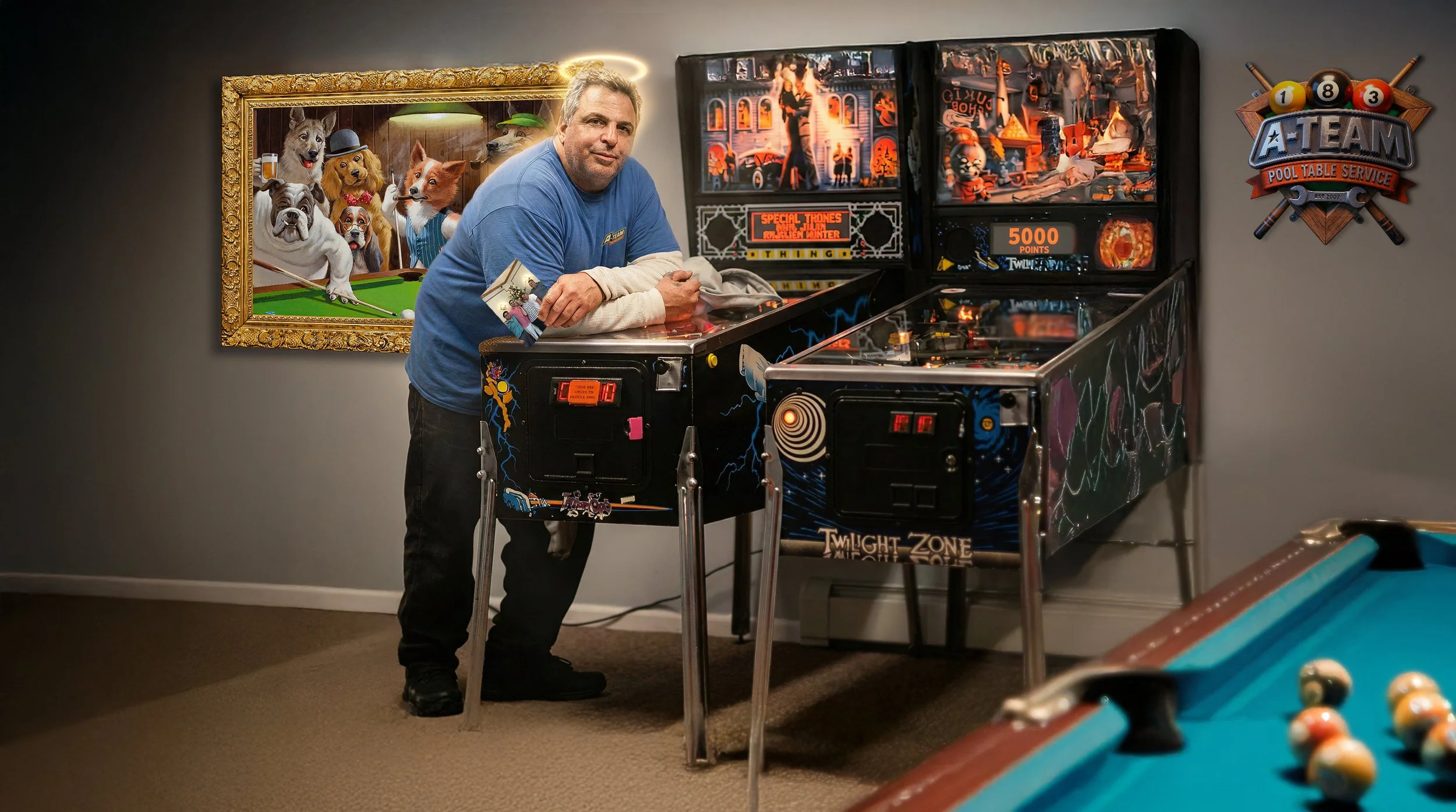 A man with a halo effect standing next to a Twilight Zone themed pinball machine, with a framed painting of dogs playing pool on the wall behind him, and a pool table in the foreground.
