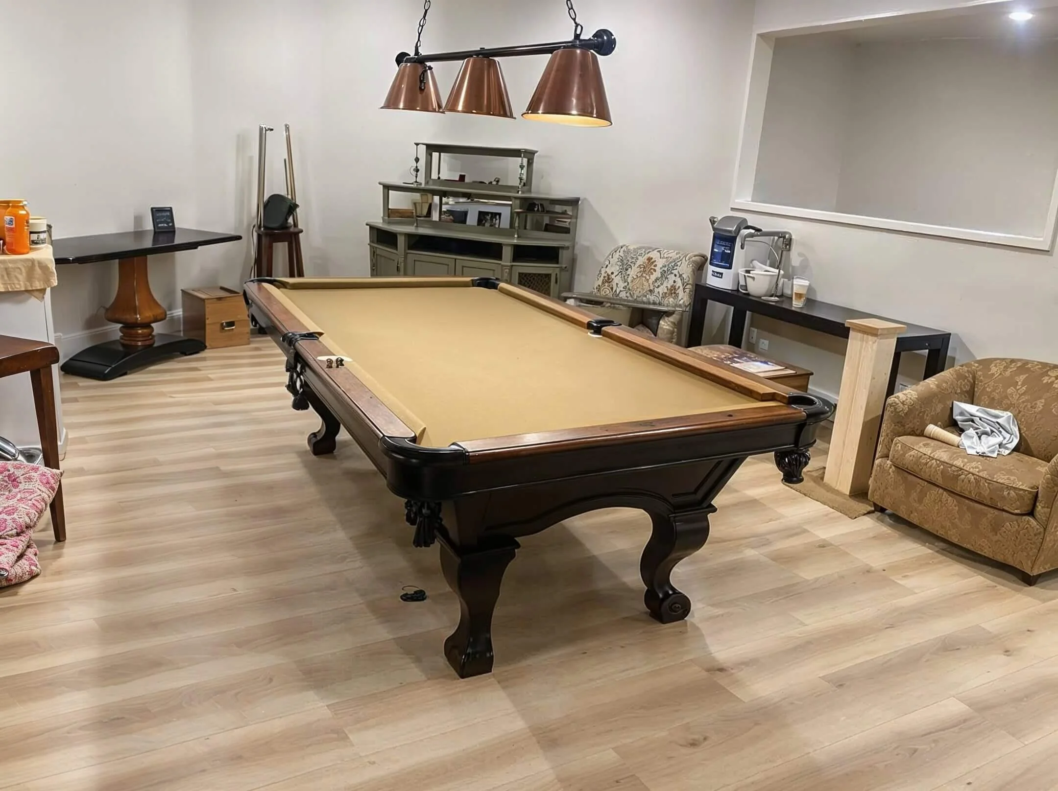 A room with a pool table at the center surrounded by various furniture including a brown couch, armchair, and tables, with a chandelier hanging above.