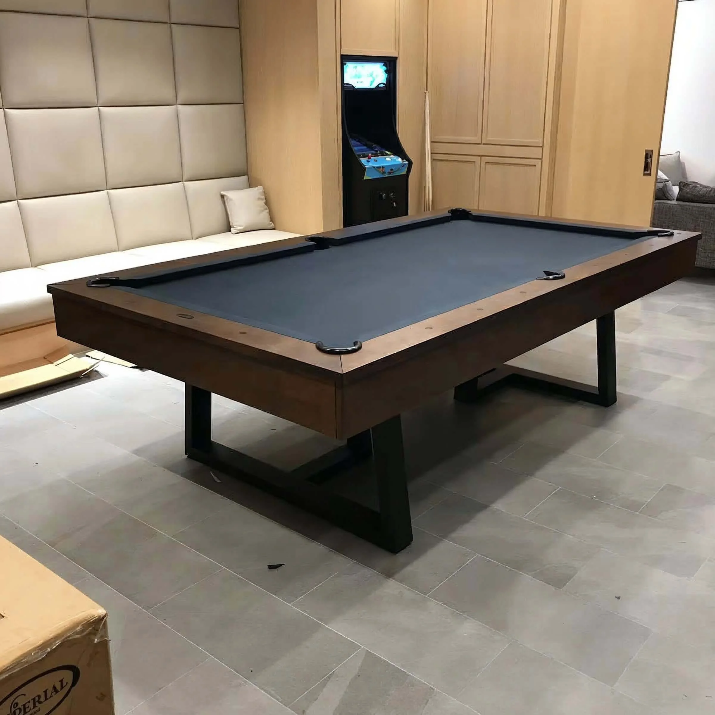 A modern indoor game room with a pool table, a white cushioned bench, and an arcade game in the background.