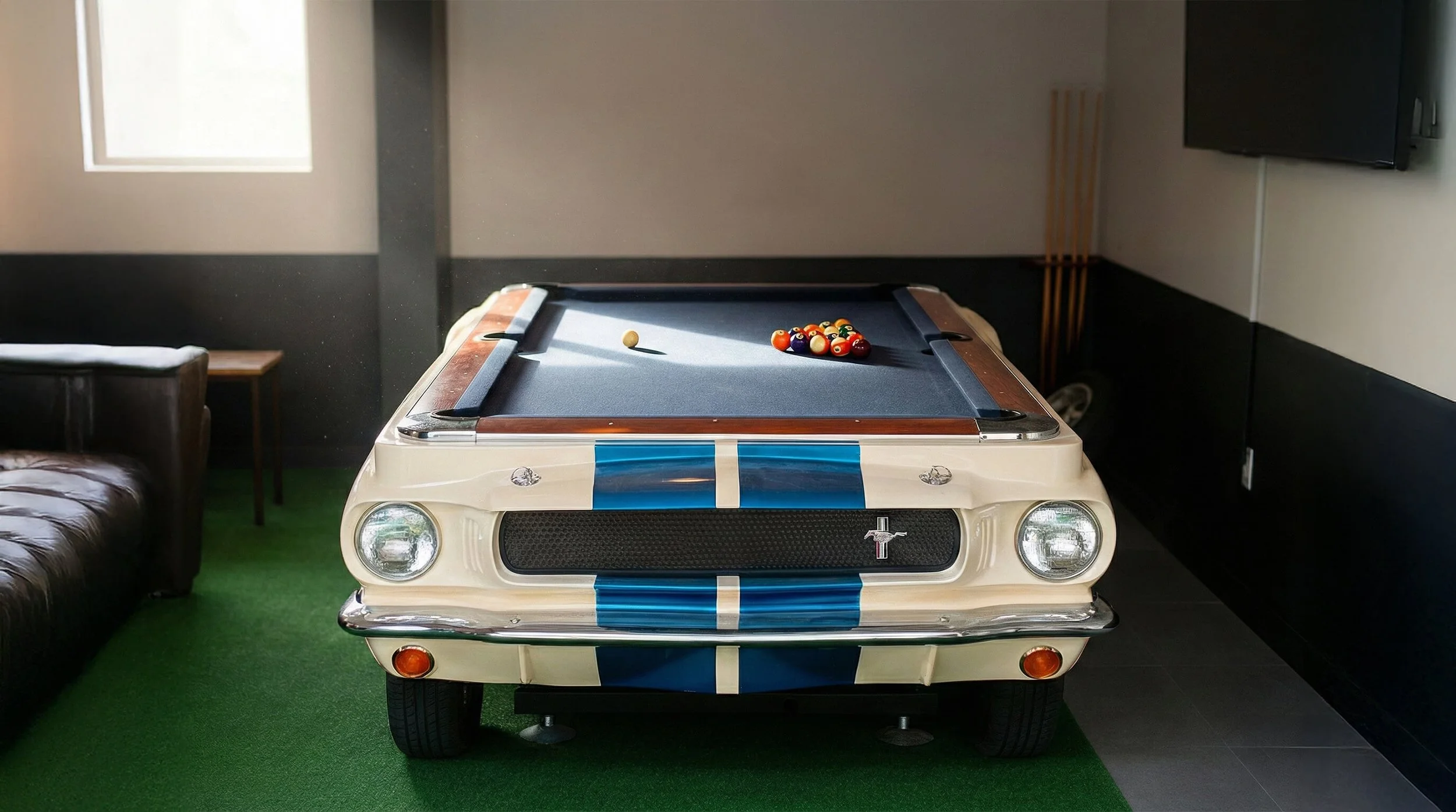 Vintage white Mustang car converted into a pool table with a blue felt surface, pool balls racked, and a cue ball on the table in a room with green carpet, brown leather sofa, and a wall-mounted television.