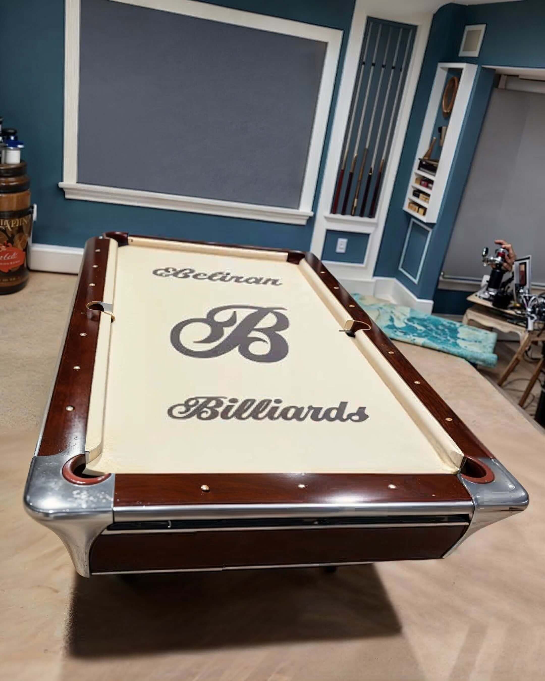 A billiards table with a custom cover displaying the text 'Beveran Billiards' and a large letter 'B' logo.