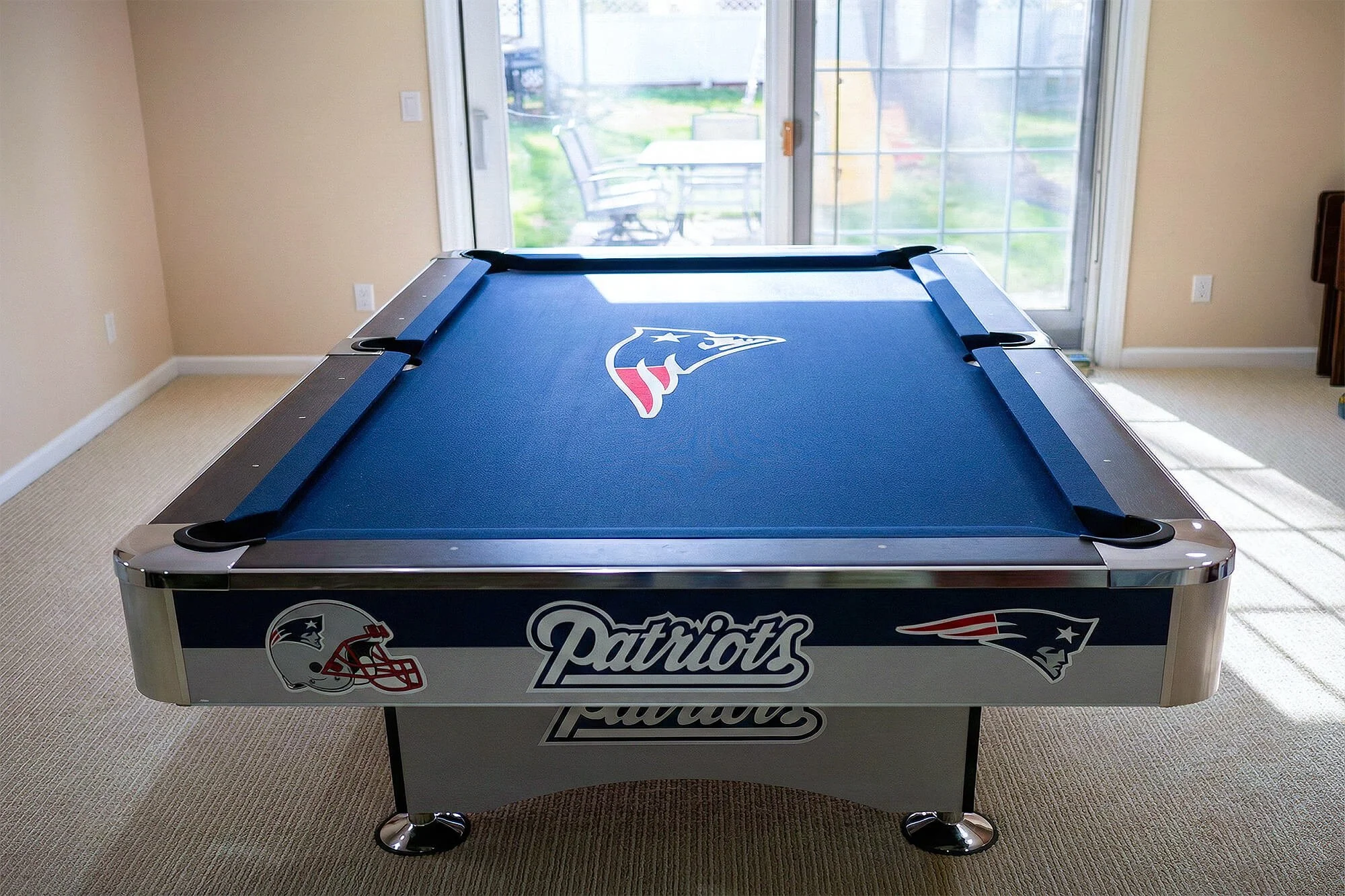 An air hockey table with New England Patriots and Houston Texans logos, located in a bright room with sliding glass doors leading outside.