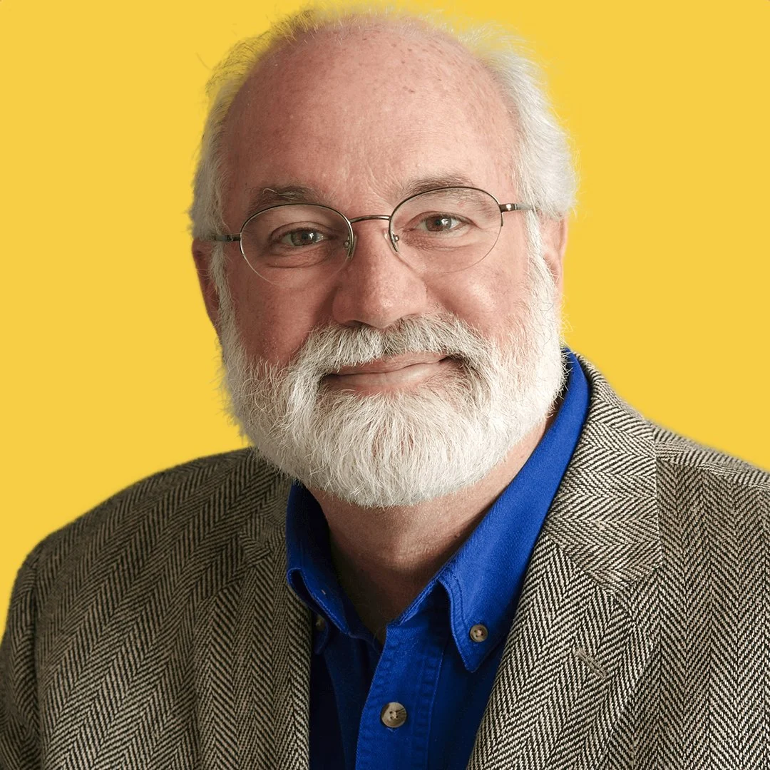 A portrait of an elderly man with a white beard, glasses, wearing a blue shirt and a brown plaid blazer, against a yellow background.