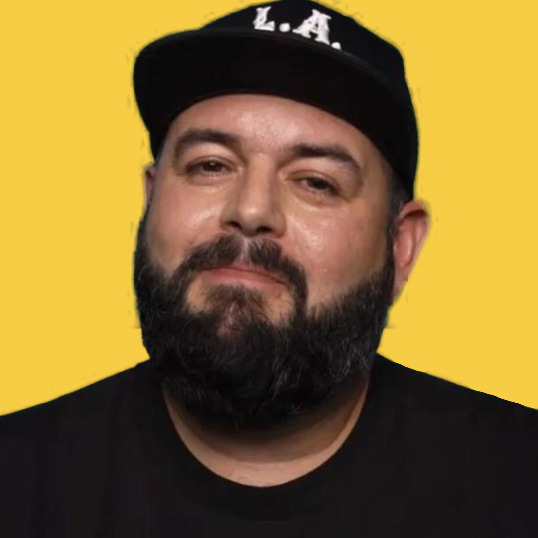 Portrait of a man with a beard wearing a black cap with white letters 'L.A.' and a black shirt, against a yellow background.