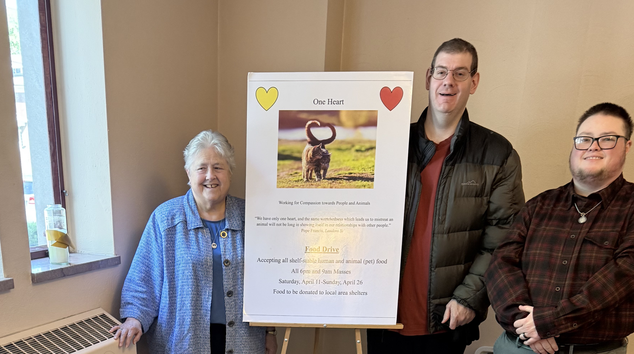 3 individuals stand by sign that reads "One Heart: Working for Compassion Towards People and Animals"