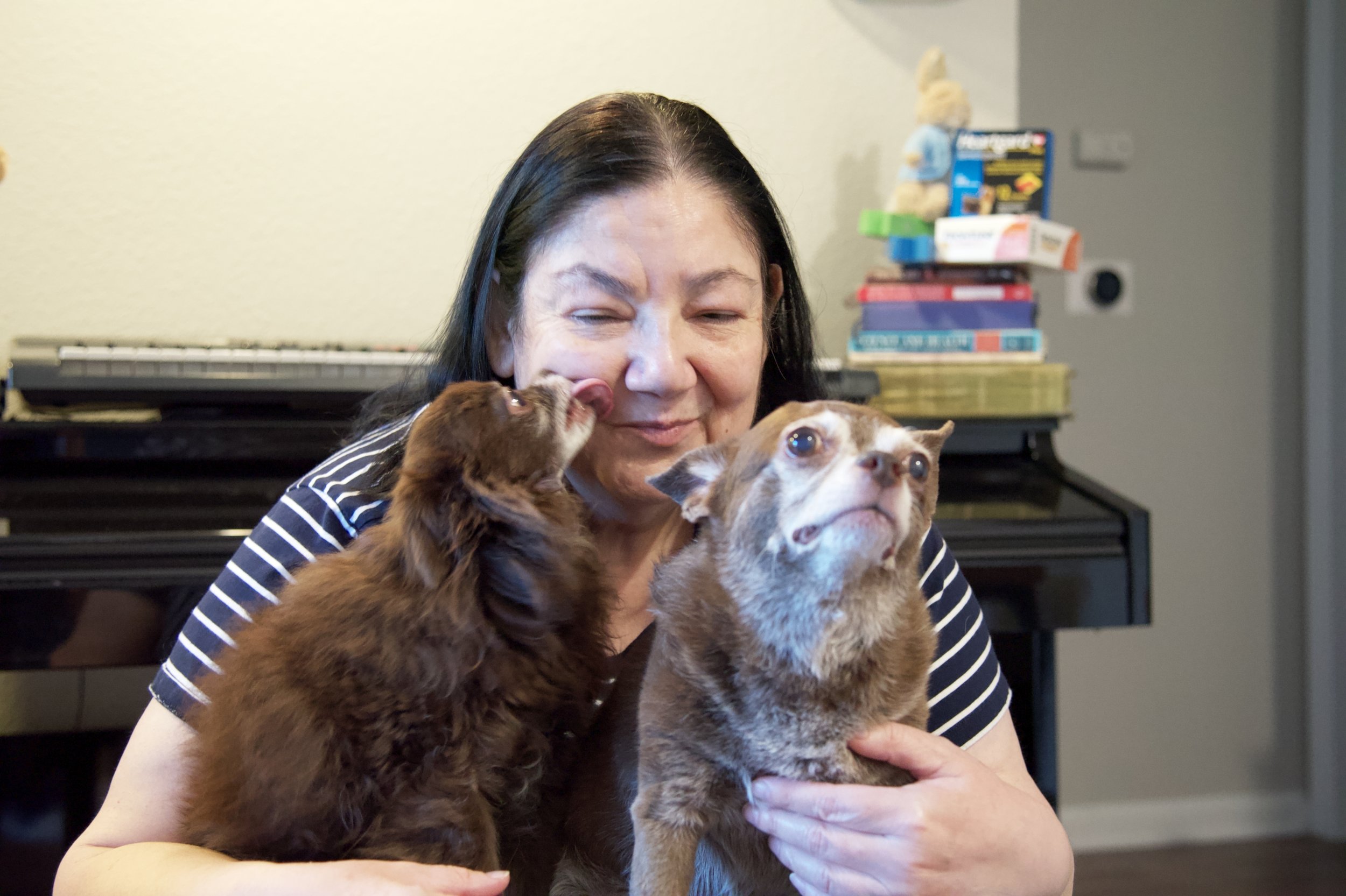 Woman smiles while holding two small brown dogs