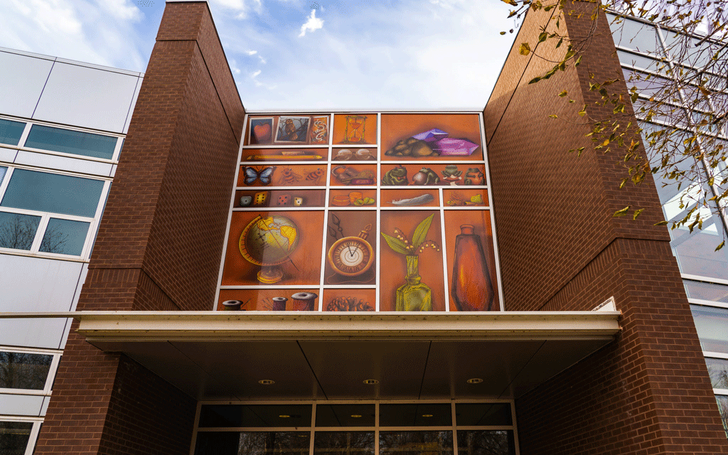 Building with red brick columns shows large decals with vases, globe, pictures, butterflies, ladybug, bees, and more, all covering windows to make them visible to birds.