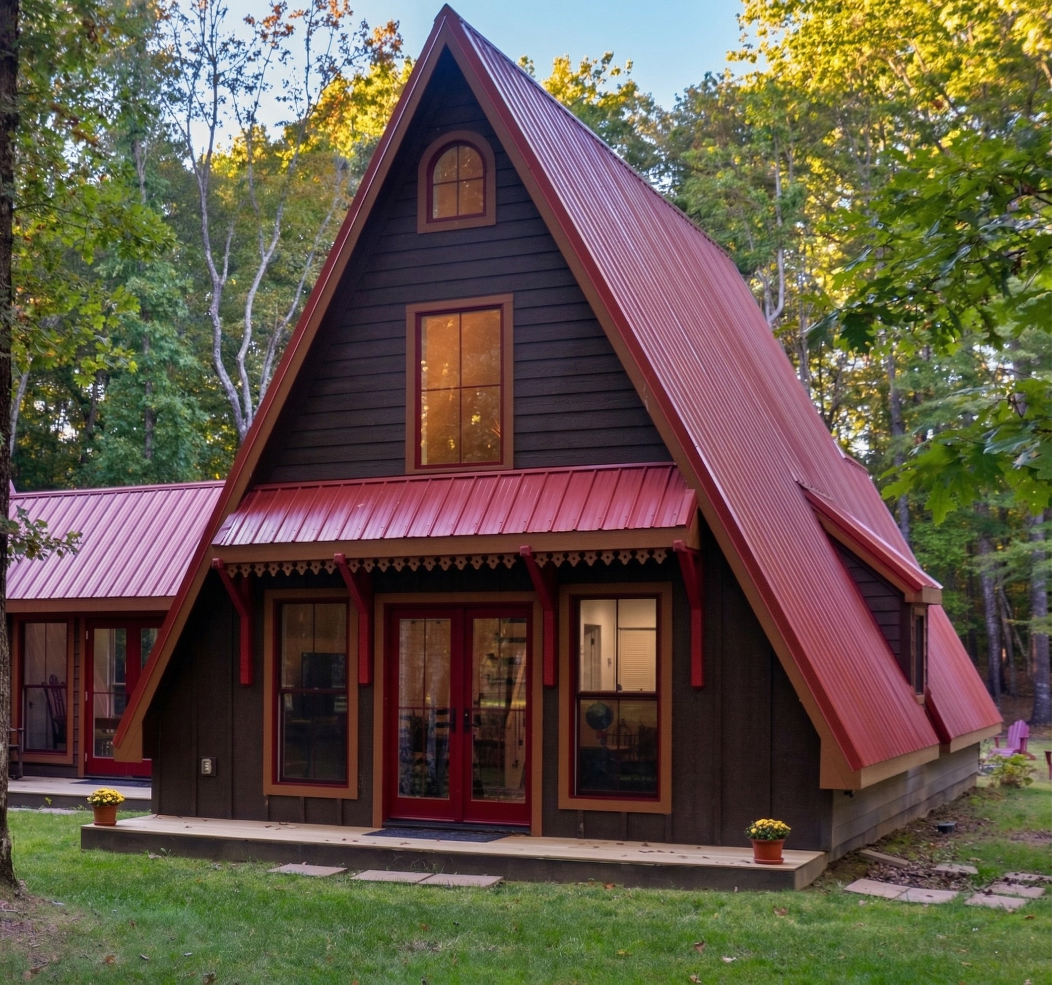 A modern A-frame house with a steep red metal roof, black wooden siding, and large windows, situated in a wooded area with trees and a small lawn.