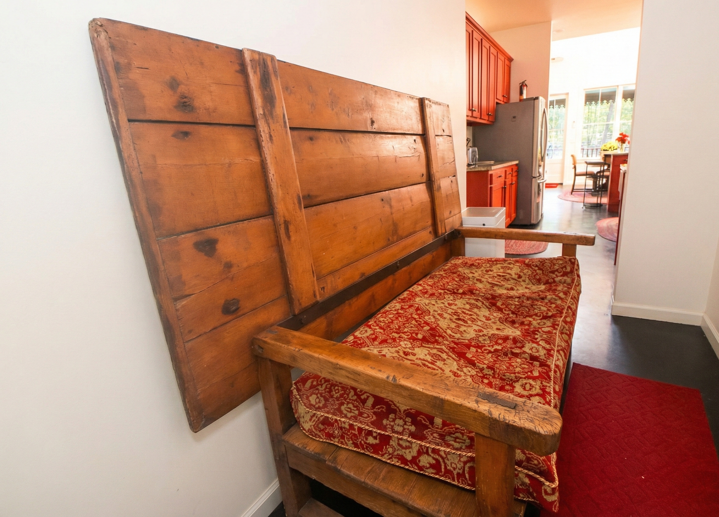 A rustic wooden headboard attached to a red and gold patterned upholstered couch in a cozy kitchen and dining area.