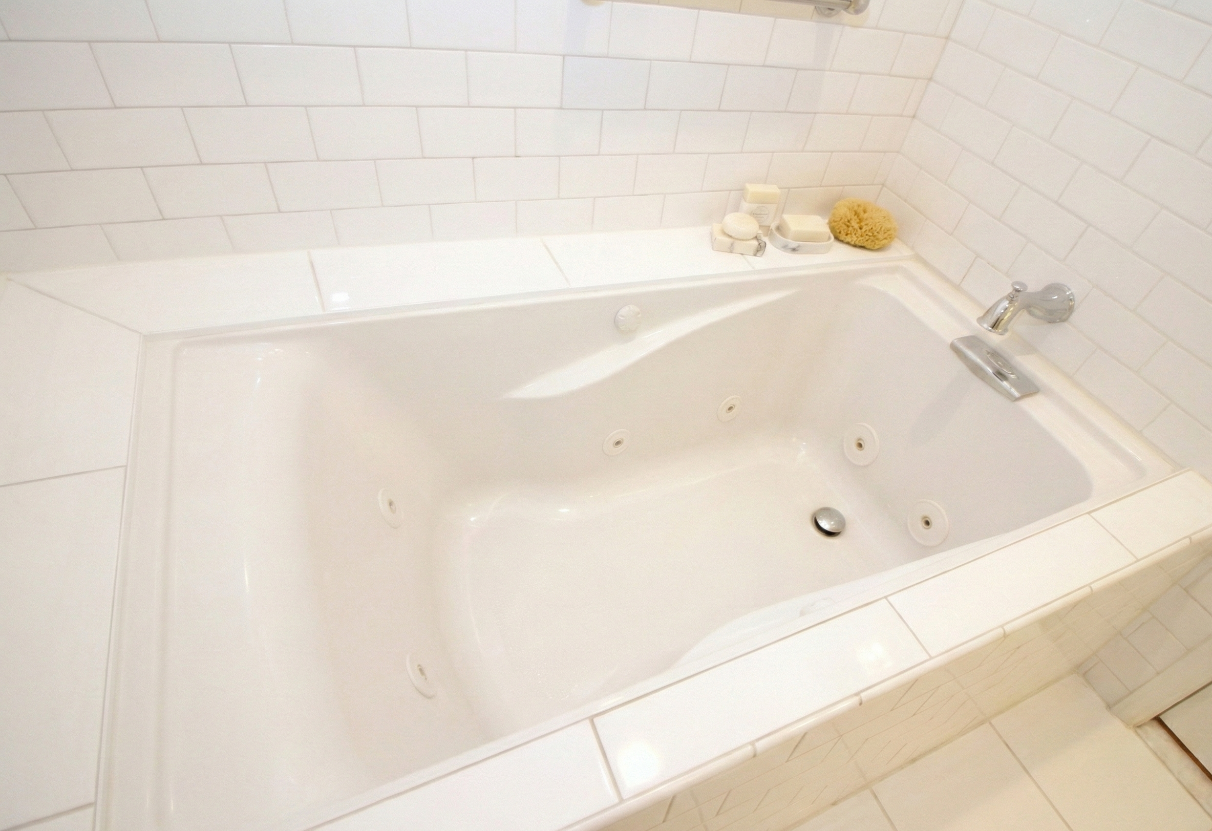 A white bathtub with multiple jets, set against a tiled wall with soap and bath accessories on the ledge.