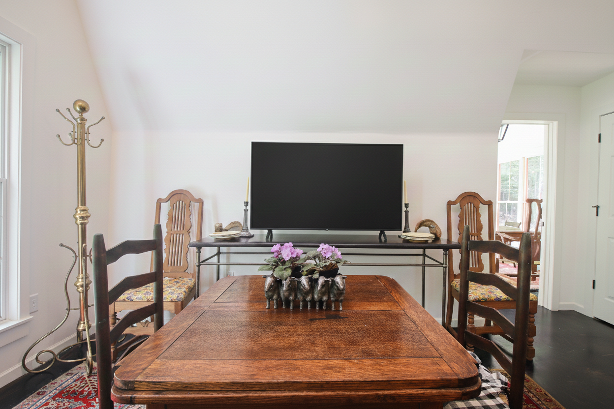 A dining room with a wooden table, four chairs, a TV on a glass table, and a flower arrangement on the table.
