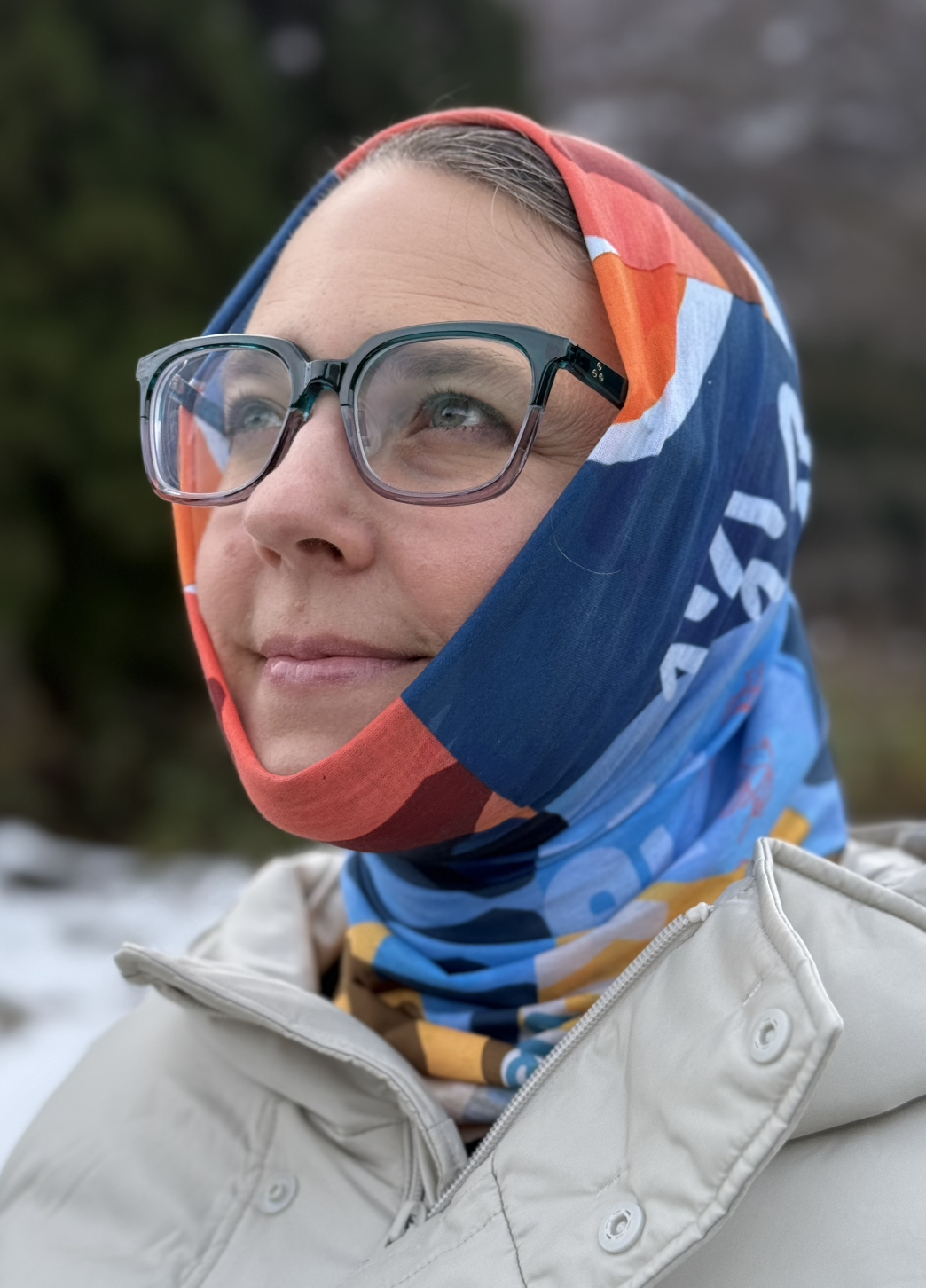 A red, blue, yellow and white geometric patterned scarf with the map of each resort in Hakuba Japan and some Japanese characters on it pulled over the head of a female skier
