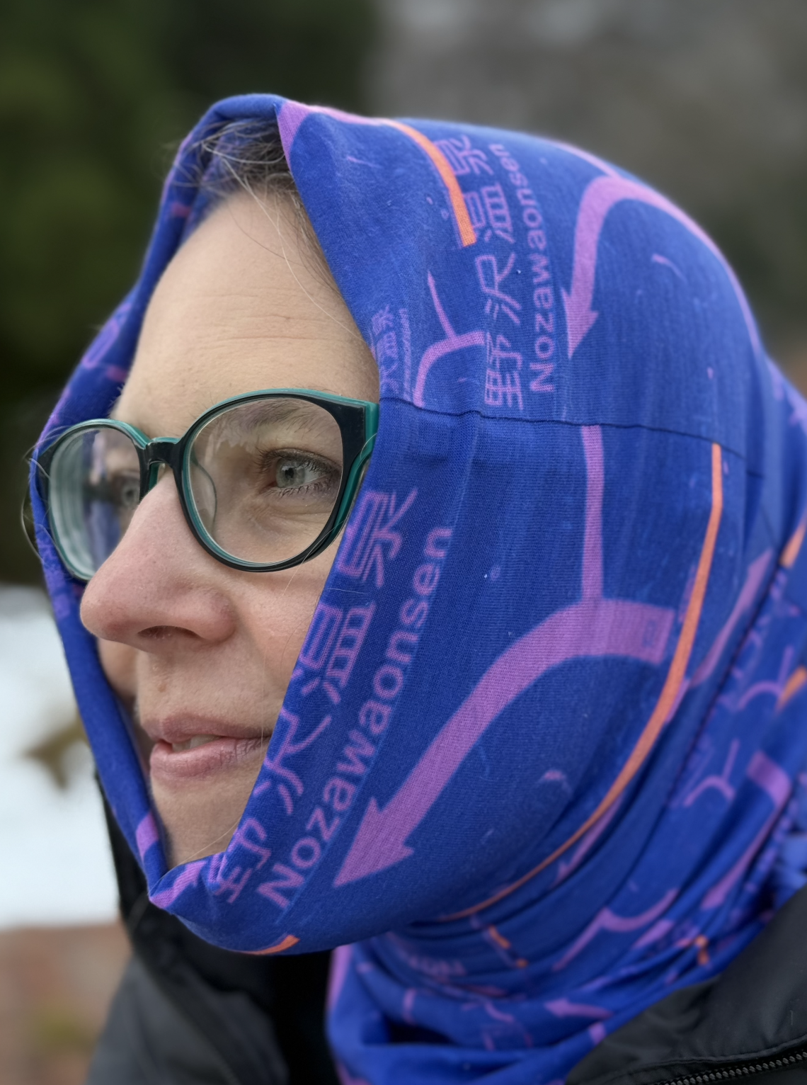 Woman wearing pink and purple grunge style ski tube scarf gathered at neck. Design features Japanese for Nozawa Onsen and the sign at the top of the gondola in the Nozawa ski resort.