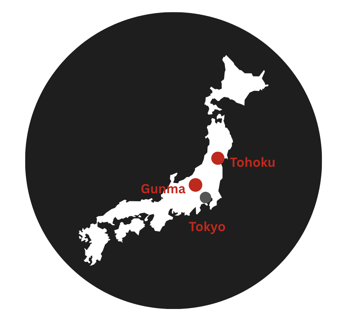 A black circle with a map of Japan on it in white. A grey dot represents the Tokyo region and two red dots represents the regions of Gunma and Tohoku.