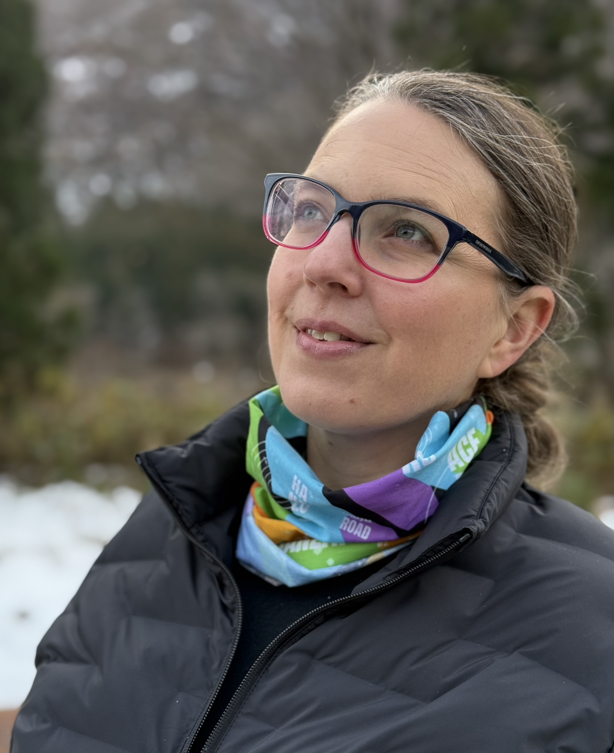 Tube ski gathered around neck of a female. Scarf has the pattern of colorful blocks with the names of ski lifts in 3D block typography with subtle line art detail.