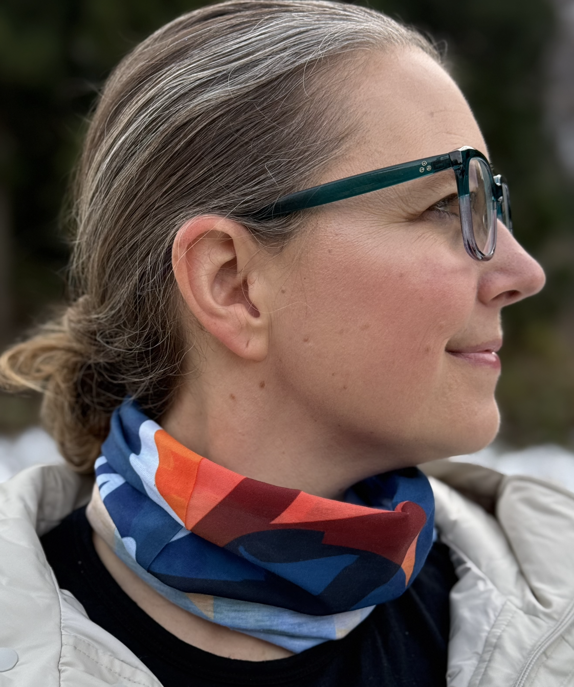 A red, blue, yellow and white geometric patterned scarf with the map of each resort in Hakuba Japan and some Japanese characters on it bunched up around the neck of a female standing outside in winter