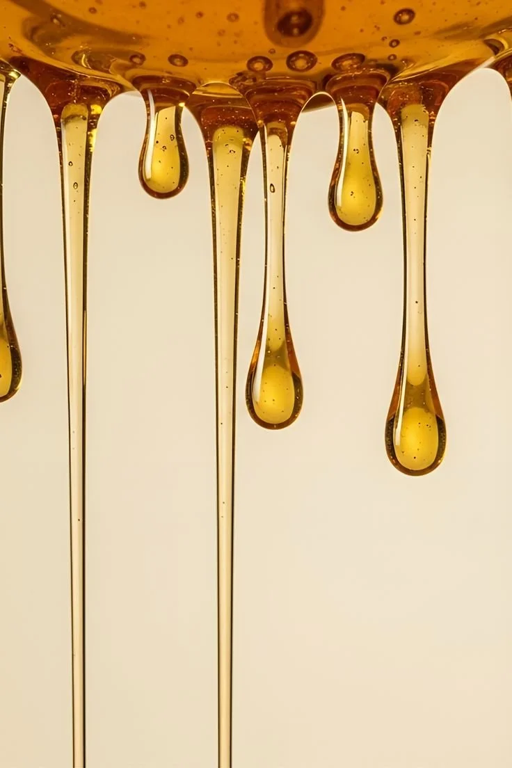 Close-up of honey dripping from a jar with a golden amber color.
